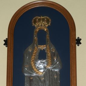 Zdjęcie nr 1: Sukienka na obraz Matki Boskiej umieszczona w przeszklonej gablocie w kształcie stojącego prostokąta, zamkniętego łukiem półkolistym. Suknia Matki Boskiej z długimi rękawami ułożonymi na piersi w geście modlitwy, u szyi dekorowana ozdobną bordiurą. Płaszcz założony na głowę, ciasno oplatający sylwetkę zdobiony na brzegu złoconą bordiurą. Suknia i płaszcz dekorowane 12 złoconymi gwiazdkami oraz dwoma równoramiennymi krzyżykami na ramionach Matki Boskiej. U dołu półksiężyc i obłoki, a na głowie zamknięta korona, wysadzana różnokolorowymi kamieniami. Bordiury, gwiazdki, krzyżyki i korona złocone, pozostałe elementy srebrzone. Rama drewniana, profilowana i malowana w kolorze brązu. Tło ciemnoniebieskie.