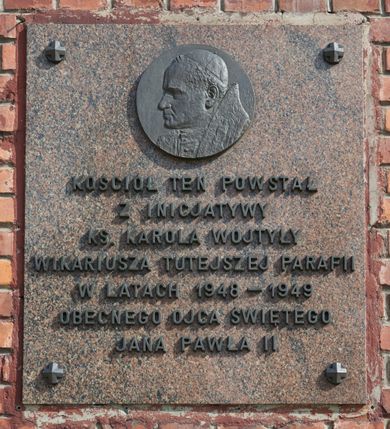 Zdjęcie nr 8: Kościół nieorientowany, skierowany prezbiterium ku północy, otoczony metalowym ogrodzeniem.  
Nawa na planie prostokąta z delikatnie wysuniętymi ramionami transeptu i z węższym oraz niższym prezbiterium, zamkniętym półkoliście, z wieżą dostawioną od fasady. Wzdłuż nawy dwuprzęsłowe arkady-kaplice, sklepione i połączone przejściami. Do wschodniego ramiona transeptu przylega kaplica Chrystusa Miłosiernego na planie prostokąta z absydą. Nawa i prezbiterium sklepione kolebkowo. Otwory okienne wysokie, zamknięte półkoliście, różnej wielkości. W prezbiterium sześć okien, w arkadach bocznych pięć, a w nawie głównej, powyżej gzymsu po sześć mniejszych na każdej ze ścian. Bryła znacznie rozczłonkowana z licznymi dobudówkami o przenikających się dachach. Nawa główna nakryta dachem dwupołaciowym, a dobudówki pulpitowymi, nałożonymi na zdwojone, wysokie okna nawy. Całą budowlę obiega gzyms podokapowy, a wokół nawy kostkowy. Wieża nakryta jest ośmiokrotnie podciętym hełmem i zwieńczona małym krzyżykiem.