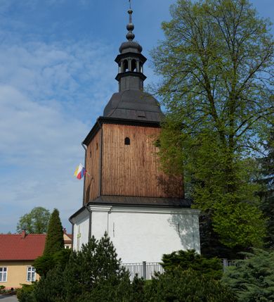 Zdjęcie nr 6: Kościół nieorientowany, skierowany prezbiterium ku północy, otoczony metalowym ogrodzeniem.  
Nawa na planie prostokąta z delikatnie wysuniętymi ramionami transeptu i z węższym oraz niższym prezbiterium, zamkniętym półkoliście, z wieżą dostawioną od fasady. Wzdłuż nawy dwuprzęsłowe arkady-kaplice, sklepione i połączone przejściami. Do wschodniego ramiona transeptu przylega kaplica Chrystusa Miłosiernego na planie prostokąta z absydą. Nawa i prezbiterium sklepione kolebkowo. Otwory okienne wysokie, zamknięte półkoliście, różnej wielkości. W prezbiterium sześć okien, w arkadach bocznych pięć, a w nawie głównej, powyżej gzymsu po sześć mniejszych na każdej ze ścian. Bryła znacznie rozczłonkowana z licznymi dobudówkami o przenikających się dachach. Nawa główna nakryta dachem dwupołaciowym, a dobudówki pulpitowymi, nałożonymi na zdwojone, wysokie okna nawy. Całą budowlę obiega gzyms podokapowy, a wokół nawy kostkowy. Wieża nakryta jest ośmiokrotnie podciętym hełmem i zwieńczona małym krzyżykiem.