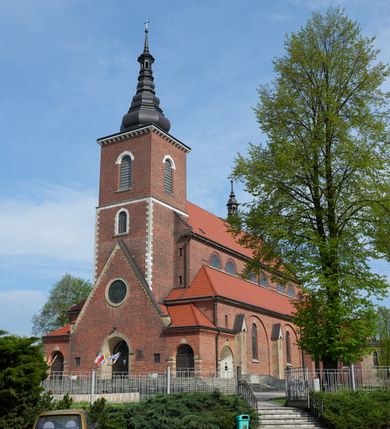 Zdjęcie nr 2: Kościół nieorientowany, skierowany prezbiterium ku północy, otoczony metalowym ogrodzeniem.  
Nawa na planie prostokąta z delikatnie wysuniętymi ramionami transeptu i z węższym oraz niższym prezbiterium, zamkniętym półkoliście, z wieżą dostawioną od fasady. Wzdłuż nawy dwuprzęsłowe arkady-kaplice, sklepione i połączone przejściami. Do wschodniego ramiona transeptu przylega kaplica Chrystusa Miłosiernego na planie prostokąta z absydą. Nawa i prezbiterium sklepione kolebkowo. Otwory okienne wysokie, zamknięte półkoliście, różnej wielkości. W prezbiterium sześć okien, w arkadach bocznych pięć, a w nawie głównej, powyżej gzymsu po sześć mniejszych na każdej ze ścian. Bryła znacznie rozczłonkowana z licznymi dobudówkami o przenikających się dachach. Nawa główna nakryta dachem dwupołaciowym, a dobudówki pulpitowymi, nałożonymi na zdwojone, wysokie okna nawy. Całą budowlę obiega gzyms podokapowy, a wokół nawy kostkowy. Wieża nakryta jest ośmiokrotnie podciętym hełmem i zwieńczona małym krzyżykiem.