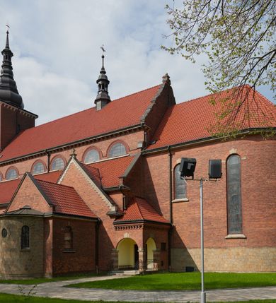 Zdjęcie nr 5: Kościół nieorientowany, skierowany prezbiterium ku północy, otoczony metalowym ogrodzeniem.  
Nawa na planie prostokąta z delikatnie wysuniętymi ramionami transeptu i z węższym oraz niższym prezbiterium, zamkniętym półkoliście, z wieżą dostawioną od fasady. Wzdłuż nawy dwuprzęsłowe arkady-kaplice, sklepione i połączone przejściami. Do wschodniego ramiona transeptu przylega kaplica Chrystusa Miłosiernego na planie prostokąta z absydą. Nawa i prezbiterium sklepione kolebkowo. Otwory okienne wysokie, zamknięte półkoliście, różnej wielkości. W prezbiterium sześć okien, w arkadach bocznych pięć, a w nawie głównej, powyżej gzymsu po sześć mniejszych na każdej ze ścian. Bryła znacznie rozczłonkowana z licznymi dobudówkami o przenikających się dachach. Nawa główna nakryta dachem dwupołaciowym, a dobudówki pulpitowymi, nałożonymi na zdwojone, wysokie okna nawy. Całą budowlę obiega gzyms podokapowy, a wokół nawy kostkowy. Wieża nakryta jest ośmiokrotnie podciętym hełmem i zwieńczona małym krzyżykiem.