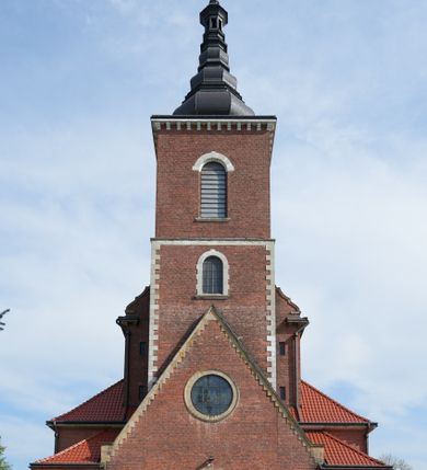 Zdjęcie nr 4: Kościół nieorientowany, skierowany prezbiterium ku północy, otoczony metalowym ogrodzeniem.  
Nawa na planie prostokąta z delikatnie wysuniętymi ramionami transeptu i z węższym oraz niższym prezbiterium, zamkniętym półkoliście, z wieżą dostawioną od fasady. Wzdłuż nawy dwuprzęsłowe arkady-kaplice, sklepione i połączone przejściami. Do wschodniego ramiona transeptu przylega kaplica Chrystusa Miłosiernego na planie prostokąta z absydą. Nawa i prezbiterium sklepione kolebkowo. Otwory okienne wysokie, zamknięte półkoliście, różnej wielkości. W prezbiterium sześć okien, w arkadach bocznych pięć, a w nawie głównej, powyżej gzymsu po sześć mniejszych na każdej ze ścian. Bryła znacznie rozczłonkowana z licznymi dobudówkami o przenikających się dachach. Nawa główna nakryta dachem dwupołaciowym, a dobudówki pulpitowymi, nałożonymi na zdwojone, wysokie okna nawy. Całą budowlę obiega gzyms podokapowy, a wokół nawy kostkowy. Wieża nakryta jest ośmiokrotnie podciętym hełmem i zwieńczona małym krzyżykiem.