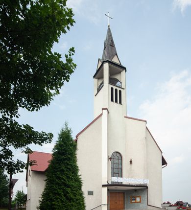 Zdjęcie nr 9: Kościół Podwyższenia Krzyża Świętego w Janowicach jest zlokalizowany na niewielkim wzniesieniu, w centrum prostokątnego placu otoczonego murowanym ogrodzeniem podzielonym na przęsła. W południowo-zachodnim narożu terenu przykościelnego usytuowana jest parawanowa dzwonnica. Kościół to budowla murowana z cegły, jednonawowa na planie krzyża łacińskiego. Do czteroprzęsłowej nawy przylega wyniesione na czterostopniowym podwyższeniu prezbiterium zamknięte prostą ścianą. Do prezbiterium od zachodu przylega zakrystia na planie zbliżonym do litery „L”, od wschodu aneks na analogicznym planie. Zakrystia skomunikowana jest z dobudowaną od południa dwukondygnacyjną i podpiwniczoną  plebanią. Wnętrze świątyni przekryte jest płaskim stropem o konstrukcji żelbetowej. Ściany w dolnej części artykułowane są za pomocą boazerii, w wyższych partiach podziały kontynuowane są w polichromii. W górnych partiach ścian (poza prezbiterium) znajdują się ukośne sufity, w nawie dodatkowo poprzedzone profilowanym gzymsem. W najwyższym rzędzie płycin mieszczą się płaskorzeźbione, stylizowane rozety z motywami geometrycznymi; analogiczne rozety zdobią parapet chóru muzycznego. Nawę doświetlają okna w kształcie stojącego prostokąta zamkniętego półkoliście: po jednym w przęsłach od drugiego do czwartego i jedno nieco większe, ponad chórem w ścianie północnej. W ścianach zamykających transept znajdują się po trzy duże otwory okienne złożone z umieszczonego po środku dużego okna w kształcie odwróconej podkowy oraz flankujących go mniejszych okien w kształcie stojącego prostokąta zamkniętego półkoliście. Główne wejście do świątyni znajduje się na osi budynku, w ścianie północnej, wejście boczne usytuowane jest w północnej ścianie zachodniego ramienia transeptu. Na szerokości pierwszego od północy przęsła nawy znajduje się chór muzyczny o konstrukcji żelbetowej, wsparty na dwóch filarach. Pod nim mieści się kruchta. Parapet chóru muzycznego jest murowany, prosty, w części środkowej trójbocznie wyłamany do wnętrza kościoła. W osi środkowej trójdzielnej fasady kościoła umieszczona wieża na planie kwadratu, nieco cofnięta w stosunku do lica elewacji, którą ujmują ukośnie ustawione ściany. Wejście do świątyni znajduje się na osi fasady. Jest zadaszone płaskim dachem; prowadzą do niego siedmiostopniowe schody. Od strony zachodniej zlokalizowany jest podjazd dla niepełnosprawnych. Otwór wejściowy ma kształt prostokąta, wewnątrz znajdują się drewniane, dwuskrzydłowe drzwi. Powyżej umiejscowione jest duże okno w kształcie stojącego prostokąta zamkniętego półkoliście. W górnej części wieży umieszczono trzy wysmukłe okna zamknięte półkoliście. W zwieńczeniu mieści się ażurowy prześwit pełniący funkcję tarasu widokowego. Wieżę wieńczy hełm w kształcie wysmukłego ostrosłupa z krzyżem. Elewacje boczne pozbawione są dekoracji.


