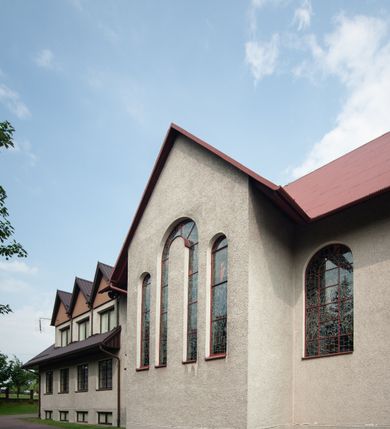 Zdjęcie nr 12: Kościół Podwyższenia Krzyża Świętego w Janowicach jest zlokalizowany na niewielkim wzniesieniu, w centrum prostokątnego placu otoczonego murowanym ogrodzeniem podzielonym na przęsła. W południowo-zachodnim narożu terenu przykościelnego usytuowana jest parawanowa dzwonnica. Kościół to budowla murowana z cegły, jednonawowa na planie krzyża łacińskiego. Do czteroprzęsłowej nawy przylega wyniesione na czterostopniowym podwyższeniu prezbiterium zamknięte prostą ścianą. Do prezbiterium od zachodu przylega zakrystia na planie zbliżonym do litery „L”, od wschodu aneks na analogicznym planie. Zakrystia skomunikowana jest z dobudowaną od południa dwukondygnacyjną i podpiwniczoną  plebanią. Wnętrze świątyni przekryte jest płaskim stropem o konstrukcji żelbetowej. Ściany w dolnej części artykułowane są za pomocą boazerii, w wyższych partiach podziały kontynuowane są w polichromii. W górnych partiach ścian (poza prezbiterium) znajdują się ukośne sufity, w nawie dodatkowo poprzedzone profilowanym gzymsem. W najwyższym rzędzie płycin mieszczą się płaskorzeźbione, stylizowane rozety z motywami geometrycznymi; analogiczne rozety zdobią parapet chóru muzycznego. Nawę doświetlają okna w kształcie stojącego prostokąta zamkniętego półkoliście: po jednym w przęsłach od drugiego do czwartego i jedno nieco większe, ponad chórem w ścianie północnej. W ścianach zamykających transept znajdują się po trzy duże otwory okienne złożone z umieszczonego po środku dużego okna w kształcie odwróconej podkowy oraz flankujących go mniejszych okien w kształcie stojącego prostokąta zamkniętego półkoliście. Główne wejście do świątyni znajduje się na osi budynku, w ścianie północnej, wejście boczne usytuowane jest w północnej ścianie zachodniego ramienia transeptu. Na szerokości pierwszego od północy przęsła nawy znajduje się chór muzyczny o konstrukcji żelbetowej, wsparty na dwóch filarach. Pod nim mieści się kruchta. Parapet chóru muzycznego jest murowany, prosty, w części środkowej trójbocznie wyłamany do wnętrza kościoła. W osi środkowej trójdzielnej fasady kościoła umieszczona wieża na planie kwadratu, nieco cofnięta w stosunku do lica elewacji, którą ujmują ukośnie ustawione ściany. Wejście do świątyni znajduje się na osi fasady. Jest zadaszone płaskim dachem; prowadzą do niego siedmiostopniowe schody. Od strony zachodniej zlokalizowany jest podjazd dla niepełnosprawnych. Otwór wejściowy ma kształt prostokąta, wewnątrz znajdują się drewniane, dwuskrzydłowe drzwi. Powyżej umiejscowione jest duże okno w kształcie stojącego prostokąta zamkniętego półkoliście. W górnej części wieży umieszczono trzy wysmukłe okna zamknięte półkoliście. W zwieńczeniu mieści się ażurowy prześwit pełniący funkcję tarasu widokowego. Wieżę wieńczy hełm w kształcie wysmukłego ostrosłupa z krzyżem. Elewacje boczne pozbawione są dekoracji.


