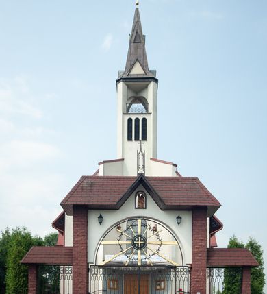 Zdjęcie nr 2: Kościół Podwyższenia Krzyża Świętego w Janowicach jest zlokalizowany na niewielkim wzniesieniu, w centrum prostokątnego placu otoczonego murowanym ogrodzeniem podzielonym na przęsła. W południowo-zachodnim narożu terenu przykościelnego usytuowana jest parawanowa dzwonnica. Kościół to budowla murowana z cegły, jednonawowa na planie krzyża łacińskiego. Do czteroprzęsłowej nawy przylega wyniesione na czterostopniowym podwyższeniu prezbiterium zamknięte prostą ścianą. Do prezbiterium od zachodu przylega zakrystia na planie zbliżonym do litery „L”, od wschodu aneks na analogicznym planie. Zakrystia skomunikowana jest z dobudowaną od południa dwukondygnacyjną i podpiwniczoną  plebanią. Wnętrze świątyni przekryte jest płaskim stropem o konstrukcji żelbetowej. Ściany w dolnej części artykułowane są za pomocą boazerii, w wyższych partiach podziały kontynuowane są w polichromii. W górnych partiach ścian (poza prezbiterium) znajdują się ukośne sufity, w nawie dodatkowo poprzedzone profilowanym gzymsem. W najwyższym rzędzie płycin mieszczą się płaskorzeźbione, stylizowane rozety z motywami geometrycznymi; analogiczne rozety zdobią parapet chóru muzycznego. Nawę doświetlają okna w kształcie stojącego prostokąta zamkniętego półkoliście: po jednym w przęsłach od drugiego do czwartego i jedno nieco większe, ponad chórem w ścianie północnej. W ścianach zamykających transept znajdują się po trzy duże otwory okienne złożone z umieszczonego po środku dużego okna w kształcie odwróconej podkowy oraz flankujących go mniejszych okien w kształcie stojącego prostokąta zamkniętego półkoliście. Główne wejście do świątyni znajduje się na osi budynku, w ścianie północnej, wejście boczne usytuowane jest w północnej ścianie zachodniego ramienia transeptu. Na szerokości pierwszego od północy przęsła nawy znajduje się chór muzyczny o konstrukcji żelbetowej, wsparty na dwóch filarach. Pod nim mieści się kruchta. Parapet chóru muzycznego jest murowany, prosty, w części środkowej trójbocznie wyłamany do wnętrza kościoła. W osi środkowej trójdzielnej fasady kościoła umieszczona wieża na planie kwadratu, nieco cofnięta w stosunku do lica elewacji, którą ujmują ukośnie ustawione ściany. Wejście do świątyni znajduje się na osi fasady. Jest zadaszone płaskim dachem; prowadzą do niego siedmiostopniowe schody. Od strony zachodniej zlokalizowany jest podjazd dla niepełnosprawnych. Otwór wejściowy ma kształt prostokąta, wewnątrz znajdują się drewniane, dwuskrzydłowe drzwi. Powyżej umiejscowione jest duże okno w kształcie stojącego prostokąta zamkniętego półkoliście. W górnej części wieży umieszczono trzy wysmukłe okna zamknięte półkoliście. W zwieńczeniu mieści się ażurowy prześwit pełniący funkcję tarasu widokowego. Wieżę wieńczy hełm w kształcie wysmukłego ostrosłupa z krzyżem. Elewacje boczne pozbawione są dekoracji.


