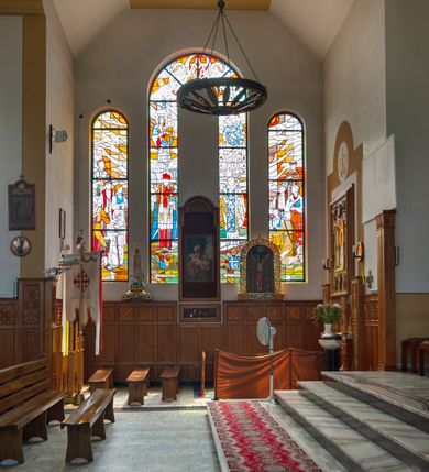 Zdjęcie nr 4: Kościół Podwyższenia Krzyża Świętego w Janowicach jest zlokalizowany na niewielkim wzniesieniu, w centrum prostokątnego placu otoczonego murowanym ogrodzeniem podzielonym na przęsła. W południowo-zachodnim narożu terenu przykościelnego usytuowana jest parawanowa dzwonnica. Kościół to budowla murowana z cegły, jednonawowa na planie krzyża łacińskiego. Do czteroprzęsłowej nawy przylega wyniesione na czterostopniowym podwyższeniu prezbiterium zamknięte prostą ścianą. Do prezbiterium od zachodu przylega zakrystia na planie zbliżonym do litery „L”, od wschodu aneks na analogicznym planie. Zakrystia skomunikowana jest z dobudowaną od południa dwukondygnacyjną i podpiwniczoną  plebanią. Wnętrze świątyni przekryte jest płaskim stropem o konstrukcji żelbetowej. Ściany w dolnej części artykułowane są za pomocą boazerii, w wyższych partiach podziały kontynuowane są w polichromii. W górnych partiach ścian (poza prezbiterium) znajdują się ukośne sufity, w nawie dodatkowo poprzedzone profilowanym gzymsem. W najwyższym rzędzie płycin mieszczą się płaskorzeźbione, stylizowane rozety z motywami geometrycznymi; analogiczne rozety zdobią parapet chóru muzycznego. Nawę doświetlają okna w kształcie stojącego prostokąta zamkniętego półkoliście: po jednym w przęsłach od drugiego do czwartego i jedno nieco większe, ponad chórem w ścianie północnej. W ścianach zamykających transept znajdują się po trzy duże otwory okienne złożone z umieszczonego po środku dużego okna w kształcie odwróconej podkowy oraz flankujących go mniejszych okien w kształcie stojącego prostokąta zamkniętego półkoliście. Główne wejście do świątyni znajduje się na osi budynku, w ścianie północnej, wejście boczne usytuowane jest w północnej ścianie zachodniego ramienia transeptu. Na szerokości pierwszego od północy przęsła nawy znajduje się chór muzyczny o konstrukcji żelbetowej, wsparty na dwóch filarach. Pod nim mieści się kruchta. Parapet chóru muzycznego jest murowany, prosty, w części środkowej trójbocznie wyłamany do wnętrza kościoła. W osi środkowej trójdzielnej fasady kościoła umieszczona wieża na planie kwadratu, nieco cofnięta w stosunku do lica elewacji, którą ujmują ukośnie ustawione ściany. Wejście do świątyni znajduje się na osi fasady. Jest zadaszone płaskim dachem; prowadzą do niego siedmiostopniowe schody. Od strony zachodniej zlokalizowany jest podjazd dla niepełnosprawnych. Otwór wejściowy ma kształt prostokąta, wewnątrz znajdują się drewniane, dwuskrzydłowe drzwi. Powyżej umiejscowione jest duże okno w kształcie stojącego prostokąta zamkniętego półkoliście. W górnej części wieży umieszczono trzy wysmukłe okna zamknięte półkoliście. W zwieńczeniu mieści się ażurowy prześwit pełniący funkcję tarasu widokowego. Wieżę wieńczy hełm w kształcie wysmukłego ostrosłupa z krzyżem. Elewacje boczne pozbawione są dekoracji.


