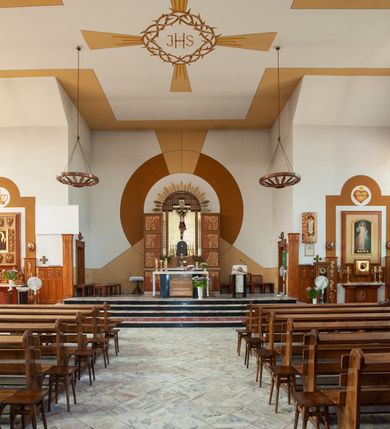 Zdjęcie nr 14: Kościół Podwyższenia Krzyża Świętego w Janowicach jest zlokalizowany na niewielkim wzniesieniu, w centrum prostokątnego placu otoczonego murowanym ogrodzeniem podzielonym na przęsła. W południowo-zachodnim narożu terenu przykościelnego usytuowana jest parawanowa dzwonnica. Kościół to budowla murowana z cegły, jednonawowa na planie krzyża łacińskiego. Do czteroprzęsłowej nawy przylega wyniesione na czterostopniowym podwyższeniu prezbiterium zamknięte prostą ścianą. Do prezbiterium od zachodu przylega zakrystia na planie zbliżonym do litery „L”, od wschodu aneks na analogicznym planie. Zakrystia skomunikowana jest z dobudowaną od południa dwukondygnacyjną i podpiwniczoną  plebanią. Wnętrze świątyni przekryte jest płaskim stropem o konstrukcji żelbetowej. Ściany w dolnej części artykułowane są za pomocą boazerii, w wyższych partiach podziały kontynuowane są w polichromii. W górnych partiach ścian (poza prezbiterium) znajdują się ukośne sufity, w nawie dodatkowo poprzedzone profilowanym gzymsem. W najwyższym rzędzie płycin mieszczą się płaskorzeźbione, stylizowane rozety z motywami geometrycznymi; analogiczne rozety zdobią parapet chóru muzycznego. Nawę doświetlają okna w kształcie stojącego prostokąta zamkniętego półkoliście: po jednym w przęsłach od drugiego do czwartego i jedno nieco większe, ponad chórem w ścianie północnej. W ścianach zamykających transept znajdują się po trzy duże otwory okienne złożone z umieszczonego po środku dużego okna w kształcie odwróconej podkowy oraz flankujących go mniejszych okien w kształcie stojącego prostokąta zamkniętego półkoliście. Główne wejście do świątyni znajduje się na osi budynku, w ścianie północnej, wejście boczne usytuowane jest w północnej ścianie zachodniego ramienia transeptu. Na szerokości pierwszego od północy przęsła nawy znajduje się chór muzyczny o konstrukcji żelbetowej, wsparty na dwóch filarach. Pod nim mieści się kruchta. Parapet chóru muzycznego jest murowany, prosty, w części środkowej trójbocznie wyłamany do wnętrza kościoła. W osi środkowej trójdzielnej fasady kościoła umieszczona wieża na planie kwadratu, nieco cofnięta w stosunku do lica elewacji, którą ujmują ukośnie ustawione ściany. Wejście do świątyni znajduje się na osi fasady. Jest zadaszone płaskim dachem; prowadzą do niego siedmiostopniowe schody. Od strony zachodniej zlokalizowany jest podjazd dla niepełnosprawnych. Otwór wejściowy ma kształt prostokąta, wewnątrz znajdują się drewniane, dwuskrzydłowe drzwi. Powyżej umiejscowione jest duże okno w kształcie stojącego prostokąta zamkniętego półkoliście. W górnej części wieży umieszczono trzy wysmukłe okna zamknięte półkoliście. W zwieńczeniu mieści się ażurowy prześwit pełniący funkcję tarasu widokowego. Wieżę wieńczy hełm w kształcie wysmukłego ostrosłupa z krzyżem. Elewacje boczne pozbawione są dekoracji.


