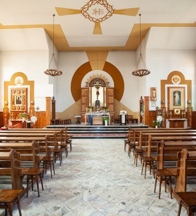 Zdjęcie nr 13: Kościół Podwyższenia Krzyża Świętego w Janowicach jest zlokalizowany na niewielkim wzniesieniu, w centrum prostokątnego placu otoczonego murowanym ogrodzeniem podzielonym na przęsła. W południowo-zachodnim narożu terenu przykościelnego usytuowana jest parawanowa dzwonnica. Kościół to budowla murowana z cegły, jednonawowa na planie krzyża łacińskiego. Do czteroprzęsłowej nawy przylega wyniesione na czterostopniowym podwyższeniu prezbiterium zamknięte prostą ścianą. Do prezbiterium od zachodu przylega zakrystia na planie zbliżonym do litery „L”, od wschodu aneks na analogicznym planie. Zakrystia skomunikowana jest z dobudowaną od południa dwukondygnacyjną i podpiwniczoną  plebanią. Wnętrze świątyni przekryte jest płaskim stropem o konstrukcji żelbetowej. Ściany w dolnej części artykułowane są za pomocą boazerii, w wyższych partiach podziały kontynuowane są w polichromii. W górnych partiach ścian (poza prezbiterium) znajdują się ukośne sufity, w nawie dodatkowo poprzedzone profilowanym gzymsem. W najwyższym rzędzie płycin mieszczą się płaskorzeźbione, stylizowane rozety z motywami geometrycznymi; analogiczne rozety zdobią parapet chóru muzycznego. Nawę doświetlają okna w kształcie stojącego prostokąta zamkniętego półkoliście: po jednym w przęsłach od drugiego do czwartego i jedno nieco większe, ponad chórem w ścianie północnej. W ścianach zamykających transept znajdują się po trzy duże otwory okienne złożone z umieszczonego po środku dużego okna w kształcie odwróconej podkowy oraz flankujących go mniejszych okien w kształcie stojącego prostokąta zamkniętego półkoliście. Główne wejście do świątyni znajduje się na osi budynku, w ścianie północnej, wejście boczne usytuowane jest w północnej ścianie zachodniego ramienia transeptu. Na szerokości pierwszego od północy przęsła nawy znajduje się chór muzyczny o konstrukcji żelbetowej, wsparty na dwóch filarach. Pod nim mieści się kruchta. Parapet chóru muzycznego jest murowany, prosty, w części środkowej trójbocznie wyłamany do wnętrza kościoła. W osi środkowej trójdzielnej fasady kościoła umieszczona wieża na planie kwadratu, nieco cofnięta w stosunku do lica elewacji, którą ujmują ukośnie ustawione ściany. Wejście do świątyni znajduje się na osi fasady. Jest zadaszone płaskim dachem; prowadzą do niego siedmiostopniowe schody. Od strony zachodniej zlokalizowany jest podjazd dla niepełnosprawnych. Otwór wejściowy ma kształt prostokąta, wewnątrz znajdują się drewniane, dwuskrzydłowe drzwi. Powyżej umiejscowione jest duże okno w kształcie stojącego prostokąta zamkniętego półkoliście. W górnej części wieży umieszczono trzy wysmukłe okna zamknięte półkoliście. W zwieńczeniu mieści się ażurowy prześwit pełniący funkcję tarasu widokowego. Wieżę wieńczy hełm w kształcie wysmukłego ostrosłupa z krzyżem. Elewacje boczne pozbawione są dekoracji.


