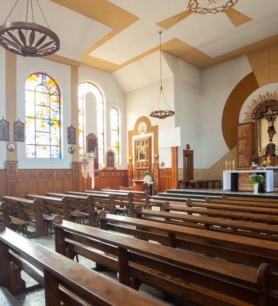 Zdjęcie nr 16: Kościół Podwyższenia Krzyża Świętego w Janowicach jest zlokalizowany na niewielkim wzniesieniu, w centrum prostokątnego placu otoczonego murowanym ogrodzeniem podzielonym na przęsła. W południowo-zachodnim narożu terenu przykościelnego usytuowana jest parawanowa dzwonnica. Kościół to budowla murowana z cegły, jednonawowa na planie krzyża łacińskiego. Do czteroprzęsłowej nawy przylega wyniesione na czterostopniowym podwyższeniu prezbiterium zamknięte prostą ścianą. Do prezbiterium od zachodu przylega zakrystia na planie zbliżonym do litery „L”, od wschodu aneks na analogicznym planie. Zakrystia skomunikowana jest z dobudowaną od południa dwukondygnacyjną i podpiwniczoną  plebanią. Wnętrze świątyni przekryte jest płaskim stropem o konstrukcji żelbetowej. Ściany w dolnej części artykułowane są za pomocą boazerii, w wyższych partiach podziały kontynuowane są w polichromii. W górnych partiach ścian (poza prezbiterium) znajdują się ukośne sufity, w nawie dodatkowo poprzedzone profilowanym gzymsem. W najwyższym rzędzie płycin mieszczą się płaskorzeźbione, stylizowane rozety z motywami geometrycznymi; analogiczne rozety zdobią parapet chóru muzycznego. Nawę doświetlają okna w kształcie stojącego prostokąta zamkniętego półkoliście: po jednym w przęsłach od drugiego do czwartego i jedno nieco większe, ponad chórem w ścianie północnej. W ścianach zamykających transept znajdują się po trzy duże otwory okienne złożone z umieszczonego po środku dużego okna w kształcie odwróconej podkowy oraz flankujących go mniejszych okien w kształcie stojącego prostokąta zamkniętego półkoliście. Główne wejście do świątyni znajduje się na osi budynku, w ścianie północnej, wejście boczne usytuowane jest w północnej ścianie zachodniego ramienia transeptu. Na szerokości pierwszego od północy przęsła nawy znajduje się chór muzyczny o konstrukcji żelbetowej, wsparty na dwóch filarach. Pod nim mieści się kruchta. Parapet chóru muzycznego jest murowany, prosty, w części środkowej trójbocznie wyłamany do wnętrza kościoła. W osi środkowej trójdzielnej fasady kościoła umieszczona wieża na planie kwadratu, nieco cofnięta w stosunku do lica elewacji, którą ujmują ukośnie ustawione ściany. Wejście do świątyni znajduje się na osi fasady. Jest zadaszone płaskim dachem; prowadzą do niego siedmiostopniowe schody. Od strony zachodniej zlokalizowany jest podjazd dla niepełnosprawnych. Otwór wejściowy ma kształt prostokąta, wewnątrz znajdują się drewniane, dwuskrzydłowe drzwi. Powyżej umiejscowione jest duże okno w kształcie stojącego prostokąta zamkniętego półkoliście. W górnej części wieży umieszczono trzy wysmukłe okna zamknięte półkoliście. W zwieńczeniu mieści się ażurowy prześwit pełniący funkcję tarasu widokowego. Wieżę wieńczy hełm w kształcie wysmukłego ostrosłupa z krzyżem. Elewacje boczne pozbawione są dekoracji.


