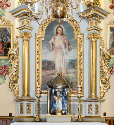 Zdjęcie nr 1: Obraz w kształcie stojącego prostokąta ukazujący stojącego frontalnie Chrystusa. Prawa ręka ułożona w geście błogosławieństwa, lewa wskazuje na promienie odchodzące od piersi. Chrystus ubrany w długą, białą tunikę. Twarz okolona długimi, jasnobrązowymi włosami i krótką, rozwidloną brodą. W tle daleki pagórkowaty krajobraz. 