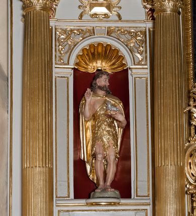 Zdjęcie nr 8: Nastawa ołtarzowa architektoniczna skomponowana na schemacie łuku triumfalnego, trójosiowa, jednokondygnacyjna ze zwieńczeniem. Ołtarz kamienny, licowany marmurowymi płytkami, z kamienną mensą. Oś środkowa jest dwukrotnie wyższa od bocznych i szersza, zamknięta półkoliście. Osie boczne ujęte dwiema parami pilastrów i stojących przed nimi kolumn o kanelowanych trzonach i kapitelach kompozytowych; między nimi nisze zwieńczone konchą z figurami św. Jana Chrzciciela i św. Jana Ewangelisty. Podpory dźwigają dwustrefowe belkowanie – niższe pełne, wyższe niepełne, delikatnie wyłamane na ich linii. Oś środkową ujmują woluty z figurami aniołów spływające na belkowanie osi bocznych; na skraju postumenty z figurami św. Floriana i św. Wacława(?). Postumenty kolumn dekorowane z trzech stron płycinami, od frontu z uskrzydlonymi główkami anielskimi; pomiędzy nimi rollwerki  z podpisami figur. Podłucze osi środkowej dekorowane kasetonami z rozetami; archiwolta wypełniona akantem, zwieńczona kluczem; w przyłuczach dwie płaskorzeźbione figury kobiece. Powyżej fryz dekorowany dużych rozmiarów uskrzydloną głową anielską, ujętą wicią roślinną, na gzymsie kartusz. W polu przyczółka roślinny postument podtrzymujący dwie uskrzydlone główki anielskie. W przyłuczach konch osi bocznych ornament roślinny, powyżej rauty, u spodu figur festony. Spód belkowania dekorowany kasetonami z rozetami. Fryzy dwóch stref belkowania wypełnione ornamentem roślinnym i rozetami; na wewnętrznym boku drugiej strefy para herbów Radwan. W polu środkowym obraz ukazujący Zwiastowanie Najświętszej Marii Panny, a na zasuwie Św. Michała Archanioła. Struktura polichromowana na szaro; kolumny, ornamentyka i profile złocone.
