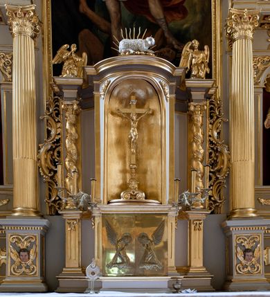 Zdjęcie nr 14: Nastawa ołtarzowa architektoniczna skomponowana na schemacie łuku triumfalnego, trójosiowa, jednokondygnacyjna ze zwieńczeniem. Ołtarz kamienny, licowany marmurowymi płytkami, z kamienną mensą. Oś środkowa jest dwukrotnie wyższa od bocznych i szersza, zamknięta półkoliście. Osie boczne ujęte dwiema parami pilastrów i stojących przed nimi kolumn o kanelowanych trzonach i kapitelach kompozytowych; między nimi nisze zwieńczone konchą z figurami św. Jana Chrzciciela i św. Jana Ewangelisty. Podpory dźwigają dwustrefowe belkowanie – niższe pełne, wyższe niepełne, delikatnie wyłamane na ich linii. Oś środkową ujmują woluty z figurami aniołów spływające na belkowanie osi bocznych; na skraju postumenty z figurami św. Floriana i św. Wacława(?). Postumenty kolumn dekorowane z trzech stron płycinami, od frontu z uskrzydlonymi główkami anielskimi; pomiędzy nimi rollwerki  z podpisami figur. Podłucze osi środkowej dekorowane kasetonami z rozetami; archiwolta wypełniona akantem, zwieńczona kluczem; w przyłuczach dwie płaskorzeźbione figury kobiece. Powyżej fryz dekorowany dużych rozmiarów uskrzydloną głową anielską, ujętą wicią roślinną, na gzymsie kartusz. W polu przyczółka roślinny postument podtrzymujący dwie uskrzydlone główki anielskie. W przyłuczach konch osi bocznych ornament roślinny, powyżej rauty, u spodu figur festony. Spód belkowania dekorowany kasetonami z rozetami. Fryzy dwóch stref belkowania wypełnione ornamentem roślinnym i rozetami; na wewnętrznym boku drugiej strefy para herbów Radwan. W polu środkowym obraz ukazujący Zwiastowanie Najświętszej Marii Panny, a na zasuwie Św. Michała Archanioła. Struktura polichromowana na szaro; kolumny, ornamentyka i profile złocone.
