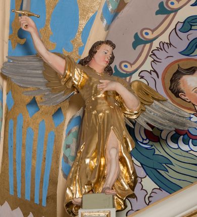 Zdjęcie nr 26: Nastawa ołtarzowa architektoniczna skomponowana na schemacie łuku triumfalnego, trójosiowa, jednokondygnacyjna ze zwieńczeniem. Ołtarz kamienny, licowany marmurowymi płytkami, z kamienną mensą. Oś środkowa jest dwukrotnie wyższa od bocznych i szersza, zamknięta półkoliście. Osie boczne ujęte dwiema parami pilastrów i stojących przed nimi kolumn o kanelowanych trzonach i kapitelach kompozytowych; między nimi nisze zwieńczone konchą z figurami św. Jana Chrzciciela i św. Jana Ewangelisty. Podpory dźwigają dwustrefowe belkowanie – niższe pełne, wyższe niepełne, delikatnie wyłamane na ich linii. Oś środkową ujmują woluty z figurami aniołów spływające na belkowanie osi bocznych; na skraju postumenty z figurami św. Floriana i św. Wacława(?). Postumenty kolumn dekorowane z trzech stron płycinami, od frontu z uskrzydlonymi główkami anielskimi; pomiędzy nimi rollwerki  z podpisami figur. Podłucze osi środkowej dekorowane kasetonami z rozetami; archiwolta wypełniona akantem, zwieńczona kluczem; w przyłuczach dwie płaskorzeźbione figury kobiece. Powyżej fryz dekorowany dużych rozmiarów uskrzydloną głową anielską, ujętą wicią roślinną, na gzymsie kartusz. W polu przyczółka roślinny postument podtrzymujący dwie uskrzydlone główki anielskie. W przyłuczach konch osi bocznych ornament roślinny, powyżej rauty, u spodu figur festony. Spód belkowania dekorowany kasetonami z rozetami. Fryzy dwóch stref belkowania wypełnione ornamentem roślinnym i rozetami; na wewnętrznym boku drugiej strefy para herbów Radwan. W polu środkowym obraz ukazujący Zwiastowanie Najświętszej Marii Panny, a na zasuwie Św. Michała Archanioła. Struktura polichromowana na szaro; kolumny, ornamentyka i profile złocone.
