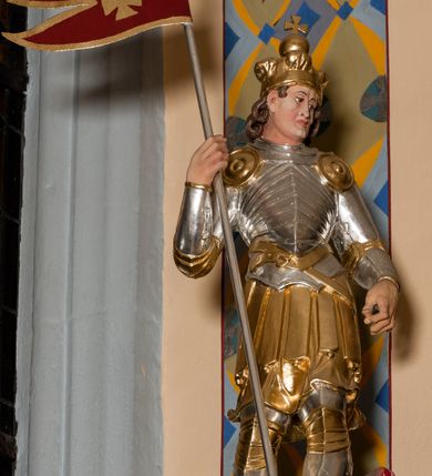 Zdjęcie nr 44: Nastawa ołtarzowa architektoniczna skomponowana na schemacie łuku triumfalnego, trójosiowa, jednokondygnacyjna ze zwieńczeniem. Ołtarz kamienny, licowany marmurowymi płytkami, z kamienną mensą. Oś środkowa jest dwukrotnie wyższa od bocznych i szersza, zamknięta półkoliście. Osie boczne ujęte dwiema parami pilastrów i stojących przed nimi kolumn o kanelowanych trzonach i kapitelach kompozytowych; między nimi nisze zwieńczone konchą z figurami św. Jana Chrzciciela i św. Jana Ewangelisty. Podpory dźwigają dwustrefowe belkowanie – niższe pełne, wyższe niepełne, delikatnie wyłamane na ich linii. Oś środkową ujmują woluty z figurami aniołów spływające na belkowanie osi bocznych; na skraju postumenty z figurami św. Floriana i św. Wacława(?). Postumenty kolumn dekorowane z trzech stron płycinami, od frontu z uskrzydlonymi główkami anielskimi; pomiędzy nimi rollwerki  z podpisami figur. Podłucze osi środkowej dekorowane kasetonami z rozetami; archiwolta wypełniona akantem, zwieńczona kluczem; w przyłuczach dwie płaskorzeźbione figury kobiece. Powyżej fryz dekorowany dużych rozmiarów uskrzydloną głową anielską, ujętą wicią roślinną, na gzymsie kartusz. W polu przyczółka roślinny postument podtrzymujący dwie uskrzydlone główki anielskie. W przyłuczach konch osi bocznych ornament roślinny, powyżej rauty, u spodu figur festony. Spód belkowania dekorowany kasetonami z rozetami. Fryzy dwóch stref belkowania wypełnione ornamentem roślinnym i rozetami; na wewnętrznym boku drugiej strefy para herbów Radwan. W polu środkowym obraz ukazujący Zwiastowanie Najświętszej Marii Panny, a na zasuwie Św. Michała Archanioła. Struktura polichromowana na szaro; kolumny, ornamentyka i profile złocone.
