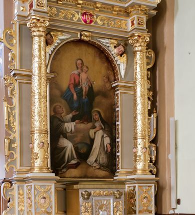 Zdjęcie nr 2: Ołtarz architektoniczny, jednoosiowy, jednokondygnacyjny ze zwieńczeniem. Antepedium z prostokątną ramą o ćwierćkoliście wyciętych narożach z promienimi i monogramem MARIA. Na mensie prostopadłościenne tabernakulum z drzwiczkami wypełnionymi płaskorzeźbionym barankiem apokaliptycznym. Wokół drzwiczek winna latorośl a w narożach uskrzydlone główki aniołków. Kompozycja nastawy wykorzystuje schemat łuku triumfalnego z arkadą zamknietą półkoliście flankowaną kolumnami stojącymi na postumentach, z kompozytowymi kapitelami dźwigającymi belkowanie. Nad belkowaniem przerwany i wyłamujący się ponad kolumnami, segmentowy przyczółek. W arkadzie obraz z Matką Boską Różąńcową ze św. Katarzyną Sieneńską i św. Dominikiem. Na zwieńczeniu dwie siedzące figury Ewangelistów (?), brodatych, ubranych w długie suknie i płaszcze, z otwartą księgą i piórem w dłoniach. W partii przerwanego przyczółka stoi na postumencie anioł z rozwartymi rękami, ubrany w długą suknię, z rozpostartymi skrzydłami. 
Cokoły zdobią motywy okuciowe z główkami aniołów. Kolumny w jednej trzeciej ujęte profilowaniem, w dolnej pokryte są okuciowymi taśmami i główkami aniołków, a w górnej wijącą się spiralnie wicią roślinną. Boki nastawy ujmują uszy utworzone z zawijających się taśm. Nad niszą z obrazem główki aniołków. Profile belkowania ozdobione konsolkami i kostkowaniem a fryz wicią roślinną i medalionem z literami IHS. Podobne ornamenty w partii przyczółka. Kolorystyka ołtarza jest szara, kolumny, profile, złocone i srebrzone, twarze aniołków i postaci w zwieńczeniu polichromowane naturalistycznie.  
