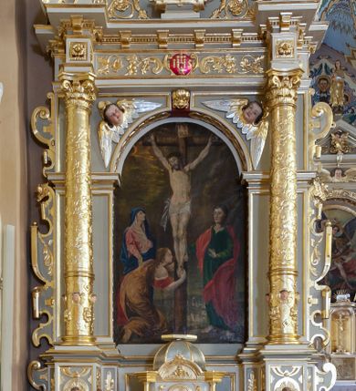 Zdjęcie nr 1: Ołtarz architektoniczny, jednoosiowy, jednokondygnacyjny ze zwieńczeniem. Antepedium z polem prostokątnym o ćwierćkolistych narożach z promianimi wypełnione literami IHS z krzyżem. Na mensie stoi tabernakulum ujęte ukośnie dostawionymi kolumnami i zwieńczone kopułką. Kompozycja nastawy wykorzystuje schemat łuku triumfalnego z arkadą zamknietą półkoliście flankowaną kolumnami stojącymi na postumentach, z kompozytowymi kapitelami dźwigającymi belkowanie. Nad belkowaniem przerwany i wyłamujący się ponad kolumnami, segmentowy przyczółek. W arkadzie obraz z ukrzyżowanym Chrystusem. Na zwieńczeniu dwie siedzące figury ewangelistów (?), brodatych, ubranych w długie suknie i płaszcze, z otwartą księgą i piórem w dłoniach. W partii przerwanego przyczółka stoi na postumencie anioł z rozwartymi rękami, ubrany w długą suknię, z rozpostartymi skrzydłami. 
Cokoły zdobią motywy okuciowe z główkami aniołów. Kolumny w jednej trzeciej ujęte profilowaniem, w dolnej pokryte są okuciowymi taśmami i główkami aniołków, a w górnej wijącą się spiralnie wicią roślinną. Boki nastawy ujmują uszy utworzone z zawijających się taśm. Nad niszą z obrazem główki aniołków. Profile belkowania ozdobione konsolkami i kostkowaniem a fryz wicią roślinną i medalionem z literami IHS. Podobne ornamenty w partii przyczółka. Kolorystyka ołtarza jest szara, kolumny, profile, złocone i srebrzone, twarze aniołków i postaci w zwieńczeniu polichromowane naturalistycznie.  
