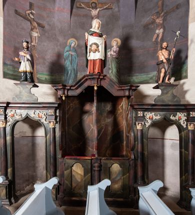 Zdjęcie nr 1: Konfesjonał do słuchania spowiedzi usznej, dwuosobowy, prostopadłościenny, od przodu z parą drzwiczek osadzonych na zawiasach, zwieńczony gzymsem pośrodku wyłamanym trójbocznie. Drzwiczki konfesjonału przedzielone kolumienką, zdobione prostokątnymi płycinami zamkniętymi łukiem półpełnym nadwieszonym. Wewnątrz siedziska oddzielone pionową ścianką o dekoracyjnym wykroju. Płyciny i tylna ściana wnętrza marmoryzowane. Po bokach dwie ścianki parawanowe z prostokątnymi zamkniętymi łukiem kotarowym bramkami dla penitentów. Bramki ujęte pilastrami o kapitelach w formie główki aniołka ze złoconymi skrzydełkami, dźwigającymi uproszczone belkowanie i gzyms występujący nad podporami. W przyłuczach bramek dekoracja malarska. Na gzymsie ustawione rzeźby pełnoplastyczne, polichromowane: w osi środkowej święta Weronika z chustą, w osiach bramek na konsolach o ozdobnym wykroju święty Jan Nepomucen (po lewej) i święty Jan Chrzciciel po prawej. 