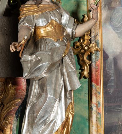 Zdjęcie nr 12: Ołtarz na rzucie połowy owalu, architektoniczny, kulisowy, jednokondygnacyjny, jednoosiowy, ze zwieńczeniem. Drewniana mensa ołtarza (późniejsza) oparta na skrzyni o formie tumby z wydzielonym cokołem. Retabulum na wysokim potrójnym, cokole, ujęte parą ukośnie ustawionych konsol o formie wolut, na których ustawione rzeźby, oraz parą odsuniętych od lica części środkowej kolumn o gładkich trzonach i kompozytowych kapitelach, wspierających przerwane belkowanie i gzyms. Pole środkowe ujęte pilastrami o wolutowych kapitelach, zwieńczone gzymsem wygiętym łukiem wklęsło-wypukłym. Pośrodku pola profilowana rama zamknięta łukiem wklęsło-wypukłym nadwieszonym, na obraz ołtarzowy. Zwieńczenie o dekoracyjnym wykroju linią wklęsło-wypukłą, z wysuniętymi na kolumny spływami wolutowymi.  Pośrodku zwieńczenia profilowana rama w kształcie stojącego owalu. Antepedium, część środkowa retabulum oraz zwieńczenie zdobione motywami ornamentów rokokowych. Retabulum ujęte parą ażurowych, rokokowych uszaków. W płycinach na spływach motywy roślinne i rozetki. Pośrodku gzymsu wieńczącego część środkową retabulum kartusz ujęty ornamentem rokokowym. W zwieńczeniu, na gzymsie, po bokach para wazonów z kwiatami, szczyt z dekoracją roccaillową. W polu środkowym obraz Objawienie się Chrystusa św. Małgorzacie Alacoque. Na wolutowych konsolach po bokach rzeźby św. Apolonii po lewej i św. Rozalii z Palermo po prawej stronie. W zwieńczeniu malowane ozdobne litery IHS z krzyżem, ujęte promienistą glorią oraz koroną cierniową. W osiach kolumn na spływach wolutowych zwieńczenia para aniołków. Na mensie trzy kanony ołtarzowe ujęte ażurowymi ramami ze stylizowanych wici akantu, zdobione rozetami. Struktura ołtarza w całości marmoryzowana, kolorystyka w odcieniach zieleni, beżów, czerwieni i niebieskim. Fragmenty detalu architektonicznego i ornamenty złocone i srebrzone. 