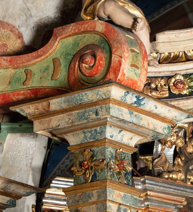 Zdjęcie nr 16: Ołtarz na rzucie połowy owalu, architektoniczny, kulisowy, jednokondygnacyjny, jednoosiowy, ze zwieńczeniem. Drewniana mensa ołtarza (późniejsza) oparta na skrzyni o formie tumby z wydzielonym cokołem. Retabulum na wysokim potrójnym, cokole, ujęte parą ukośnie ustawionych konsol o formie wolut, na których ustawione rzeźby, oraz parą odsuniętych od lica części środkowej kolumn o gładkich trzonach i kompozytowych kapitelach, wspierających przerwane belkowanie i gzyms. Pole środkowe ujęte pilastrami o wolutowych kapitelach, zwieńczone gzymsem wygiętym łukiem wklęsło-wypukłym. Pośrodku pola profilowana rama zamknięta łukiem wklęsło-wypukłym nadwieszonym, na obraz ołtarzowy. Zwieńczenie o dekoracyjnym wykroju linią wklęsło-wypukłą, z  wysuniętymi  na kolumny spływami wolutowymi.  Pośrodku zwieńczenia profilowana rama w kształcie stojącego owalu. Antepedium, część środkowa retabulum oraz zwieńczenie zdobione motywami ornamentów rokokowych. Retabulum ujęte parą ażurowych, rokokowych uszaków. W płycinach na spływach motywy roślinne i rozetki. Pośrodku gzymsu wieńczącego część środkową retabulum kartusz ujęty ornamentem rokokowym. W zwieńczeniu, na gzymsie, po bokach para wazonów z kwiatami, szczyt z dekoracją roccaillową. W polu środkowym obraz Matka Boska Różańcowa ze świętym Dominikiem. Na wolutowych konsolach po bokach rzeźby św. Joachima po lewej i św. Józefa po prawej stronie. W zwieńczeniu malowane splecione litery imienia MARIA, ujęte promienistą glorią oraz wieńcem z róż. W osiach kolumn na spływach wolutowych zwieńczenia para aniołków. Na mensie trzy kanony ołtarzowe ujęte ażurowymi ramami ze stylizowanych wici akantu, zdobione rozetami. Struktura ołtarza w całości marmoryzowana, kolorystyka w odcieniach zieleni, beżów, czerwieni i niebieskim. Fragmenty detalu architektonicznego i ornamenty złocone i srebrzone. 