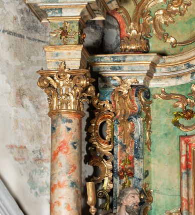 Zdjęcie nr 14: Ołtarz na rzucie połowy owalu, architektoniczny, kulisowy, jednokondygnacyjny, jednoosiowy, ze zwieńczeniem. Drewniana mensa ołtarza (późniejsza) oparta na skrzyni o formie tumby z wydzielonym cokołem. Retabulum na wysokim potrójnym, cokole, ujęte parą ukośnie ustawionych konsol o formie wolut, na których ustawione rzeźby, oraz parą odsuniętych od lica części środkowej kolumn o gładkich trzonach i kompozytowych kapitelach, wspierających przerwane belkowanie i gzyms. Pole środkowe ujęte pilastrami o wolutowych kapitelach, zwieńczone gzymsem wygiętym łukiem wklęsło-wypukłym. Pośrodku pola profilowana rama zamknięta łukiem wklęsło-wypukłym nadwieszonym, na obraz ołtarzowy. Zwieńczenie o dekoracyjnym wykroju linią wklęsło-wypukłą, z  wysuniętymi  na kolumny spływami wolutowymi.  Pośrodku zwieńczenia profilowana rama w kształcie stojącego owalu. Antepedium, część środkowa retabulum oraz zwieńczenie zdobione motywami ornamentów rokokowych. Retabulum ujęte parą ażurowych, rokokowych uszaków. W płycinach na spływach motywy roślinne i rozetki. Pośrodku gzymsu wieńczącego część środkową retabulum kartusz ujęty ornamentem rokokowym. W zwieńczeniu, na gzymsie, po bokach para wazonów z kwiatami, szczyt z dekoracją roccaillową. W polu środkowym obraz Matka Boska Różańcowa ze świętym Dominikiem. Na wolutowych konsolach po bokach rzeźby św. Joachima po lewej i św. Józefa po prawej stronie. W zwieńczeniu malowane splecione litery imienia MARIA, ujęte promienistą glorią oraz wieńcem z róż. W osiach kolumn na spływach wolutowych zwieńczenia para aniołków. Na mensie trzy kanony ołtarzowe ujęte ażurowymi ramami ze stylizowanych wici akantu, zdobione rozetami. Struktura ołtarza w całości marmoryzowana, kolorystyka w odcieniach zieleni, beżów, czerwieni i niebieskim. Fragmenty detalu architektonicznego i ornamenty złocone i srebrzone. 