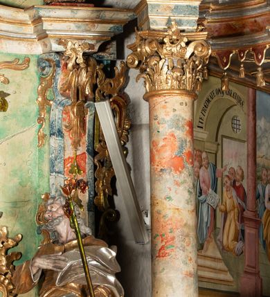 Zdjęcie nr 15: Ołtarz na rzucie połowy owalu, architektoniczny, kulisowy, jednokondygnacyjny, jednoosiowy, ze zwieńczeniem. Drewniana mensa ołtarza (późniejsza) oparta na skrzyni o formie tumby z wydzielonym cokołem. Retabulum na wysokim potrójnym, cokole, ujęte parą ukośnie ustawionych konsol o formie wolut, na których ustawione rzeźby, oraz parą odsuniętych od lica części środkowej kolumn o gładkich trzonach i kompozytowych kapitelach, wspierających przerwane belkowanie i gzyms. Pole środkowe ujęte pilastrami o wolutowych kapitelach, zwieńczone gzymsem wygiętym łukiem wklęsło-wypukłym. Pośrodku pola profilowana rama zamknięta łukiem wklęsło-wypukłym nadwieszonym, na obraz ołtarzowy. Zwieńczenie o dekoracyjnym wykroju linią wklęsło-wypukłą, z  wysuniętymi  na kolumny spływami wolutowymi.  Pośrodku zwieńczenia profilowana rama w kształcie stojącego owalu. Antepedium, część środkowa retabulum oraz zwieńczenie zdobione motywami ornamentów rokokowych. Retabulum ujęte parą ażurowych, rokokowych uszaków. W płycinach na spływach motywy roślinne i rozetki. Pośrodku gzymsu wieńczącego część środkową retabulum kartusz ujęty ornamentem rokokowym. W zwieńczeniu, na gzymsie, po bokach para wazonów z kwiatami, szczyt z dekoracją roccaillową. W polu środkowym obraz Matka Boska Różańcowa ze świętym Dominikiem. Na wolutowych konsolach po bokach rzeźby św. Joachima po lewej i św. Józefa po prawej stronie. W zwieńczeniu malowane splecione litery imienia MARIA, ujęte promienistą glorią oraz wieńcem z róż. W osiach kolumn na spływach wolutowych zwieńczenia para aniołków. Na mensie trzy kanony ołtarzowe ujęte ażurowymi ramami ze stylizowanych wici akantu, zdobione rozetami. Struktura ołtarza w całości marmoryzowana, kolorystyka w odcieniach zieleni, beżów, czerwieni i niebieskim. Fragmenty detalu architektonicznego i ornamenty złocone i srebrzone. 