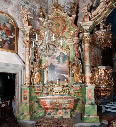 Zdjęcie nr 2: Obraz w kształcie stojącego prostokąta zwieńczonego łukiem wklęsło-wypukłym, z przedstawieniem Matki Boskiej wręczającej różaniec św. Dominikowi (Dominik Guzmán OP). Matka Boska, ukazana w całej postaci, stoi na obłokach w prawej części obrazu, ubrana w długą, białą suknię i obszerny niebieski płaszcz okrywający głowę i plecy. Lewą ręką podtrzymuje Dzieciątko Jezus, w prawej trzyma różaniec. Biodra i nóżki Dzieciątka otulone są białą szatą. W lewej rączce trzyma kulę ziemską, prawa uniesiona w geście błogosławieństwa. Wśród obłoków oraz przy płaszczu Marii ukazane aniołki. U dołu, po lewej stronie obrazu ukazany w trzech czwartych, tyłem do widza klęczący św. Dominik. Głowa lekko uniesiona do góry, wzrok skierowany w stronę Matki Boskiej, ręce rozłożone, uniesione do góry. Święty ubrany w habit dominikański i narzuconą na wierzch czarną kapę. Tło przestawienia stanowi rozległy, górzysty pejzaż z płynącą pośrodku rzeką. Kolorystyka delikatna, stonowana gama barwna. W prawym dolnym narożu sygnatura: Tary Lajos / 1912 Budapest.