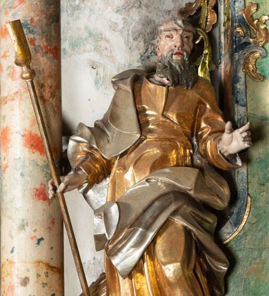 Zdjęcie nr 1: Rzeźba pełnoplastyczna, drążona od tyłu, umieszczona po lewej stronie ołtarza bocznego, przedstawiająca stojącego na niewysokim, prostopadłościennym, marmoryzowanym postumencie św. Joachima. Święty ukazany frontalnie, w kontrapoście. Głowa lekko przechylona w prawo, włosy falowane, krótkie, siwe. Twarz o wyrazistych rysach i długim siwym zaroście. Oczy zwrócone lekko ku górze, usta rozchylone. Lewa ręka świętego, zgięta w łokciu, uniesiona na wysokości talii, prawą podtrzymuje laskę pasterską. Święty ubrany w długą, złoconą tunikę i narzucony na nią srebrzony płaszcz. Fałdy szat układają się równolegle, miejscami spłaszczone, miejscami załamujące się. Spod tuniki widoczne bose stopy. 