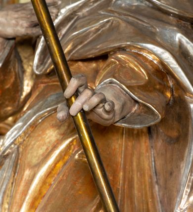 Zdjęcie nr 3: Rzeźba pełnoplastyczna, drążona od tyłu, umieszczona po prawej stronie ołtarza bocznego, przedstawia stojącego na niewysokim, prostopadłościennym, marmoryzowanym postumencie świętego Józefa. Święty ukazany frontalnie, w wyrazistym kontrapoście. Głowa lekko odchylona do tyłu i skręcona w lewo, włosy siwe, falowane, długie, opadające na plecy. Twarz o wyrazistych rysach i krótkim siwym zaroście. Oczy zwrócone w lewo ku górze. Prawa ręka świętego zgięta w łokciu, z dłonią złożoną na piersiach, lewą podtrzymuje kwitnącą różdżkę o długim drzewcu. Święty ubrany w długą, złoconą tunikę i narzucony na nią srebrzony płaszcz, przewieszony przez srebrzony pas opadający na prawe biodro. Fałdy szat układają się równolegle, miejscami spłaszczone, załamujące się. Spod tuniki widoczne stopy w srebrzone sandałach. 