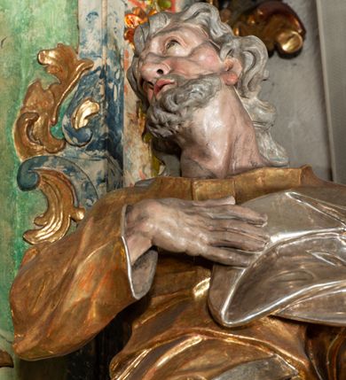 Zdjęcie nr 4: Rzeźba pełnoplastyczna, drążona od tyłu, umieszczona po prawej stronie ołtarza bocznego, przedstawia stojącego na niewysokim, prostopadłościennym, marmoryzowanym postumencie świętego Józefa. Święty ukazany frontalnie, w wyrazistym kontrapoście. Głowa lekko odchylona do tyłu i skręcona w lewo, włosy siwe, falowane, długie, opadające na plecy. Twarz o wyrazistych rysach i krótkim siwym zaroście. Oczy zwrócone w lewo ku górze. Prawa ręka świętego zgięta w łokciu, z dłonią złożoną na piersiach, lewą podtrzymuje kwitnącą różdżkę o długim drzewcu. Święty ubrany w długą, złoconą tunikę i narzucony na nią srebrzony płaszcz, przewieszony przez srebrzony pas opadający na prawe biodro. Fałdy szat układają się równolegle, miejscami spłaszczone, załamujące się. Spod tuniki widoczne stopy w srebrzone sandałach. 
