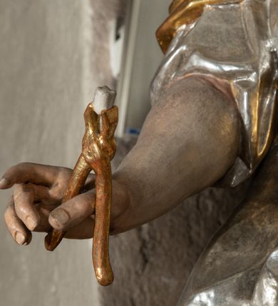 Zdjęcie nr 2: Rzeźba pełnoplastyczna, przyścienna, drążona z tyłu, przedstawiająca stojącą na niewysokim, prostopadłościennym, marmoryzowanym postumencie św. Apolonię. Święta widoczna z profilu, w wyraźnym kontrapoście i lekkim skręcie ciała. Głowa odchylona lekko do tyłu i w lewą stronę. Włosy luźno upięte w kok, z puklem opadającym na prawe ramię. Na głowie złocony diadem zdobiony trzema czerwonymi guzami. Twarz o wyrazistych rysach, wzrok skierowany ku górze. Święta ubrana w spodnią, długą, złoconą i wierzchnią, krótką, srebrzoną tunikę, krótkimi rękawami, ze złoconym gorsetem. Na plecach srebrzony płaszcz, przewieszony przez złocony pas opadający na prawe biodro. Fałdy szat równoległe, spłaszczone, załamujące się. Na stopach srebrzone buty o szpiczastych noskach. W lewej uniesionej ręce gałązka palmowa, w prawej opuszczonej i odwiedzionej w bok obcęgi z zębem. Polichromia partii ciała naturalistyczna. 