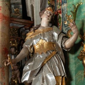 Zdjęcie nr 1: Rzeźba pełnoplastyczna, przyścienna, drążona z tyłu, przedstawiająca stojącą na niewysokim, prostopadłościennym, marmoryzowanym postumencie św. Apolonię. Święta widoczna z profilu, w wyraźnym kontrapoście i lekkim skręcie ciała. Głowa odchylona lekko do tyłu i w lewą stronę. Włosy luźno upięte w kok, z puklem opadającym na prawe ramię. Na głowie złocony diadem zdobiony trzema czerwonymi guzami. Twarz o wyrazistych rysach, wzrok skierowany ku górze. Święta ubrana w spodnią, długą, złoconą i wierzchnią, krótką, srebrzoną tunikę, krótkimi rękawami, ze złoconym gorsetem. Na plecach srebrzony płaszcz, przewieszony przez złocony pas opadający na prawe biodro. Fałdy szat równoległe, spłaszczone, załamujące się. Na stopach srebrzone buty o szpiczastych noskach. W lewej uniesionej ręce gałązka palmowa, w prawej opuszczonej i odwiedzionej w bok obcęgi z zębem. Polichromia partii ciała naturalistyczna. 