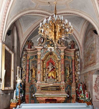 Zdjęcie nr 3: Ołtarz architektoniczny, trójosiowy, z wydzieloną częścią cokołową, jednokondygnacyjny, ze zwieńczeniem. Mensa drewniana tumbowa, ozdobiona nałożonymi płaskorzeźbionymi motywami rocaille’ów i roślinnymi. Po bokach mensy, w części cokołowej dwie bramki obejścia zamknięte półkoliście, w których osadzone na zawiasach drzwi jednoskrzydłowe z płycinami z malowanymi przedstawieniami świętych. W predelli oszklona trumienka z rzeźbą Chrystusa w grobie. Pole środkowe nastawy ujęte dwoma czworobocznymi filarami o kompozytowych kapitelach. Pola boczne wklęsłe i cofnięte od lica pola środkowego flankowane kolumnami o gładkich trzonach i kompozytowych kapitelach, umieszczonych na wysokich dwustopniowych postumentach ustawionych kątowo, zdobionych płycinami. Podpory dźwigają pełne belkowanie i gzyms, przerwane nad polem środkowym. W polu środkowym głęboka nisza w kształcie prostokąta stojącego zamkniętego łukiem wypukło-wklęsłym, w bogatym obramieniu. W niej rzeźba Pieta. Po bokach, na tle filarów, umieszczone dwa okazałe anioły w dynamicznych pozach, z rozłożonymi skrzydłami. Ponad niszą płaskorzeźbiona Chusta św. Weroniki rozpostarta przez dwa uskrzydlone putta ze stopami wspartymi na obłokach. W polach bocznych nastawy sferyczne płyciny w asymetrycznych złoconych obramieniach, na których tle umieszczone na konsolach rzeźby: Św. Jan Ewangelista (po lewej) i Św. Maria Magdalena (po prawej). Zwieńczenie w formie aedikuli ujętej wolutami i zwieńczonej półkoliście. Na tle aedikuli rzeźbione przedstawienie tronującego Boga Ojca, ponad głową którego Arma Christi; wokół putta i uskrzydlone główki aniołków. W osiach podpór rzeźby uskrzydlonych aniołów. Uszaki nastawy rzeźbione, ażurowe, złocone, z motywów rocaille’ów i kwiatów słonecznika. Struktura polichromowana na kolor szaro-niebieski, a trzony filarów i kolumn oraz tła płycin na czerwono, imitując marmur;  detale i ornamenty złocone; szaty rzeźb złocone i srebrzone; karnacje w kolorze naturalnym. 