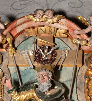 Zdjęcie nr 6: Ołtarz architektoniczny, trójosiowy, z wydzieloną częścią cokołową, jednokondygnacyjny, ze zwieńczeniem. Mensa drewniana tumbowa, ozdobiona nałożonymi płaskorzeźbionymi motywami rocaille’ów i roślinnymi. Po bokach mensy, w części cokołowej dwie bramki obejścia zamknięte półkoliście, w których osadzone na zawiasach drzwi jednoskrzydłowe z płycinami z malowanymi przedstawieniami świętych. W predelli oszklona trumienka z rzeźbą Chrystusa w grobie. Pole środkowe nastawy ujęte dwoma czworobocznymi filarami o kompozytowych kapitelach. Pola boczne wklęsłe i cofnięte od lica pola środkowego flankowane kolumnami o gładkich trzonach i kompozytowych kapitelach, umieszczonych na wysokich dwustopniowych postumentach ustawionych kątowo, zdobionych płycinami. Podpory dźwigają pełne belkowanie i gzyms, przerwane nad polem środkowym. W polu środkowym głęboka nisza w kształcie prostokąta stojącego zamkniętego łukiem wypukło-wklęsłym, w bogatym obramieniu. W niej rzeźba Pieta. Po bokach, na tle filarów, umieszczone dwa okazałe anioły w dynamicznych pozach, z rozłożonymi skrzydłami. Ponad niszą płaskorzeźbiona Chusta św. Weroniki rozpostarta przez dwa uskrzydlone putta ze stopami wspartymi na obłokach. W polach bocznych nastawy sferyczne płyciny w asymetrycznych złoconych obramieniach, na których tle umieszczone na konsolach rzeźby: Św. Jan Ewangelista (po lewej) i Św. Maria Magdalena (po prawej). Zwieńczenie w formie aedikuli ujętej wolutami i zwieńczonej półkoliście. Na tle aedikuli rzeźbione przedstawienie tronującego Boga Ojca, ponad głową którego Arma Christi; wokół putta i uskrzydlone główki aniołków. W osiach podpór rzeźby uskrzydlonych aniołów. Uszaki nastawy rzeźbione, ażurowe, złocone, z motywów rocaille’ów i kwiatów słonecznika. Struktura polichromowana na kolor szaro-niebieski, a trzony filarów i kolumn oraz tła płycin na czerwono, imitując marmur;  detale i ornamenty złocone; szaty rzeźb złocone i srebrzone; karnacje w kolorze naturalnym. 