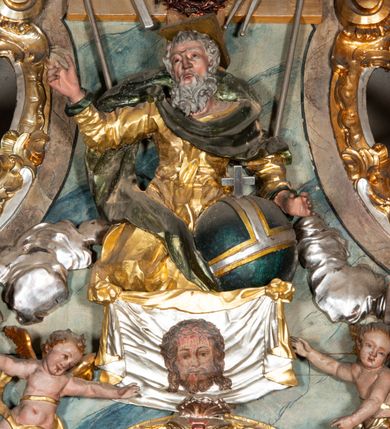 Zdjęcie nr 8: Ołtarz architektoniczny, trójosiowy, z wydzieloną częścią cokołową, jednokondygnacyjny, ze zwieńczeniem. Mensa drewniana tumbowa, ozdobiona nałożonymi płaskorzeźbionymi motywami rocaille’ów i roślinnymi. Po bokach mensy, w części cokołowej dwie bramki obejścia zamknięte półkoliście, w których osadzone na zawiasach drzwi jednoskrzydłowe z płycinami z malowanymi przedstawieniami świętych. W predelli oszklona trumienka z rzeźbą Chrystusa w grobie. Pole środkowe nastawy ujęte dwoma czworobocznymi filarami o kompozytowych kapitelach. Pola boczne wklęsłe i cofnięte od lica pola środkowego flankowane kolumnami o gładkich trzonach i kompozytowych kapitelach, umieszczonych na wysokich dwustopniowych postumentach ustawionych kątowo, zdobionych płycinami. Podpory dźwigają pełne belkowanie i gzyms, przerwane nad polem środkowym. W polu środkowym głęboka nisza w kształcie prostokąta stojącego zamkniętego łukiem wypukło-wklęsłym, w bogatym obramieniu. W niej rzeźba Pieta. Po bokach, na tle filarów, umieszczone dwa okazałe anioły w dynamicznych pozach, z rozłożonymi skrzydłami. Ponad niszą płaskorzeźbiona Chusta św. Weroniki rozpostarta przez dwa uskrzydlone putta ze stopami wspartymi na obłokach. W polach bocznych nastawy sferyczne płyciny w asymetrycznych złoconych obramieniach, na których tle umieszczone na konsolach rzeźby: Św. Jan Ewangelista (po lewej) i Św. Maria Magdalena (po prawej). Zwieńczenie w formie aedikuli ujętej wolutami i zwieńczonej półkoliście. Na tle aedikuli rzeźbione przedstawienie tronującego Boga Ojca, ponad głową którego Arma Christi; wokół putta i uskrzydlone główki aniołków. W osiach podpór rzeźby uskrzydlonych aniołów. Uszaki nastawy rzeźbione, ażurowe, złocone, z motywów rocaille’ów i kwiatów słonecznika. Struktura polichromowana na kolor szaro-niebieski, a trzony filarów i kolumn oraz tła płycin na czerwono, imitując marmur;  detale i ornamenty złocone; szaty rzeźb złocone i srebrzone; karnacje w kolorze naturalnym. 