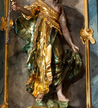 Zdjęcie nr 28: Ołtarz architektoniczny, trójosiowy, z wydzieloną częścią cokołową, jednokondygnacyjny, ze zwieńczeniem. Mensa drewniana tumbowa, ozdobiona nałożonymi płaskorzeźbionymi motywami rocaille’ów i roślinnymi. Po bokach mensy, w części cokołowej dwie bramki obejścia zamknięte półkoliście, w których osadzone na zawiasach drzwi jednoskrzydłowe z płycinami z malowanymi przedstawieniami świętych. W predelli oszklona trumienka z rzeźbą Chrystusa w grobie. Pole środkowe nastawy ujęte dwoma czworobocznymi filarami o kompozytowych kapitelach. Pola boczne wklęsłe i cofnięte od lica pola środkowego flankowane kolumnami o gładkich trzonach i kompozytowych kapitelach, umieszczonych na wysokich dwustopniowych postumentach ustawionych kątowo, zdobionych płycinami. Podpory dźwigają pełne belkowanie i gzyms, przerwane nad polem środkowym. W polu środkowym głęboka nisza w kształcie prostokąta stojącego zamkniętego łukiem wypukło-wklęsłym, w bogatym obramieniu. W niej rzeźba Pieta. Po bokach, na tle filarów, umieszczone dwa okazałe anioły w dynamicznych pozach, z rozłożonymi skrzydłami. Ponad niszą płaskorzeźbiona Chusta św. Weroniki rozpostarta przez dwa uskrzydlone putta ze stopami wspartymi na obłokach. W polach bocznych nastawy sferyczne płyciny w asymetrycznych złoconych obramieniach, na których tle umieszczone na konsolach rzeźby: Św. Jan Ewangelista (po lewej) i Św. Maria Magdalena (po prawej). Zwieńczenie w formie aedikuli ujętej wolutami i zwieńczonej półkoliście. Na tle aedikuli rzeźbione przedstawienie tronującego Boga Ojca, ponad głową którego Arma Christi; wokół putta i uskrzydlone główki aniołków. W osiach podpór rzeźby uskrzydlonych aniołów. Uszaki nastawy rzeźbione, ażurowe, złocone, z motywów rocaille’ów i kwiatów słonecznika. Struktura polichromowana na kolor szaro-niebieski, a trzony filarów i kolumn oraz tła płycin na czerwono, imitując marmur;  detale i ornamenty złocone; szaty rzeźb złocone i srebrzone; karnacje w kolorze naturalnym. 