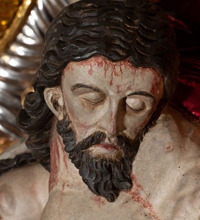 Zdjęcie nr 22: Ołtarz architektoniczny, trójosiowy, z wydzieloną częścią cokołową, jednokondygnacyjny, ze zwieńczeniem. Mensa drewniana tumbowa, ozdobiona nałożonymi płaskorzeźbionymi motywami rocaille’ów i roślinnymi. Po bokach mensy, w części cokołowej dwie bramki obejścia zamknięte półkoliście, w których osadzone na zawiasach drzwi jednoskrzydłowe z płycinami z malowanymi przedstawieniami świętych. W predelli oszklona trumienka z rzeźbą Chrystusa w grobie. Pole środkowe nastawy ujęte dwoma czworobocznymi filarami o kompozytowych kapitelach. Pola boczne wklęsłe i cofnięte od lica pola środkowego flankowane kolumnami o gładkich trzonach i kompozytowych kapitelach, umieszczonych na wysokich dwustopniowych postumentach ustawionych kątowo, zdobionych płycinami. Podpory dźwigają pełne belkowanie i gzyms, przerwane nad polem środkowym. W polu środkowym głęboka nisza w kształcie prostokąta stojącego zamkniętego łukiem wypukło-wklęsłym, w bogatym obramieniu. W niej rzeźba Pieta. Po bokach, na tle filarów, umieszczone dwa okazałe anioły w dynamicznych pozach, z rozłożonymi skrzydłami. Ponad niszą płaskorzeźbiona Chusta św. Weroniki rozpostarta przez dwa uskrzydlone putta ze stopami wspartymi na obłokach. W polach bocznych nastawy sferyczne płyciny w asymetrycznych złoconych obramieniach, na których tle umieszczone na konsolach rzeźby: Św. Jan Ewangelista (po lewej) i Św. Maria Magdalena (po prawej). Zwieńczenie w formie aedikuli ujętej wolutami i zwieńczonej półkoliście. Na tle aedikuli rzeźbione przedstawienie tronującego Boga Ojca, ponad głową którego Arma Christi; wokół putta i uskrzydlone główki aniołków. W osiach podpór rzeźby uskrzydlonych aniołów. Uszaki nastawy rzeźbione, ażurowe, złocone, z motywów rocaille’ów i kwiatów słonecznika. Struktura polichromowana na kolor szaro-niebieski, a trzony filarów i kolumn oraz tła płycin na czerwono, imitując marmur;  detale i ornamenty złocone; szaty rzeźb złocone i srebrzone; karnacje w kolorze naturalnym. 