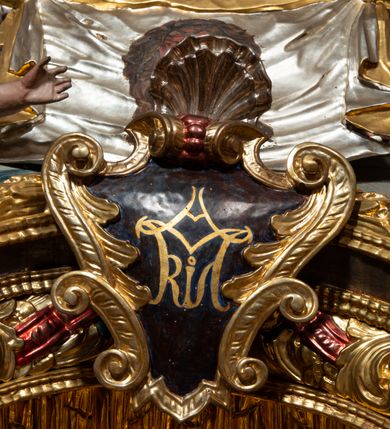 Zdjęcie nr 11: Ołtarz architektoniczny, trójosiowy, z wydzieloną częścią cokołową, jednokondygnacyjny, ze zwieńczeniem. Mensa drewniana tumbowa, ozdobiona nałożonymi płaskorzeźbionymi motywami rocaille’ów i roślinnymi. Po bokach mensy, w części cokołowej dwie bramki obejścia zamknięte półkoliście, w których osadzone na zawiasach drzwi jednoskrzydłowe z płycinami z malowanymi przedstawieniami świętych. W predelli oszklona trumienka z rzeźbą Chrystusa w grobie. Pole środkowe nastawy ujęte dwoma czworobocznymi filarami o kompozytowych kapitelach. Pola boczne wklęsłe i cofnięte od lica pola środkowego flankowane kolumnami o gładkich trzonach i kompozytowych kapitelach, umieszczonych na wysokich dwustopniowych postumentach ustawionych kątowo, zdobionych płycinami. Podpory dźwigają pełne belkowanie i gzyms, przerwane nad polem środkowym. W polu środkowym głęboka nisza w kształcie prostokąta stojącego zamkniętego łukiem wypukło-wklęsłym, w bogatym obramieniu. W niej rzeźba Pieta. Po bokach, na tle filarów, umieszczone dwa okazałe anioły w dynamicznych pozach, z rozłożonymi skrzydłami. Ponad niszą płaskorzeźbiona Chusta św. Weroniki rozpostarta przez dwa uskrzydlone putta ze stopami wspartymi na obłokach. W polach bocznych nastawy sferyczne płyciny w asymetrycznych złoconych obramieniach, na których tle umieszczone na konsolach rzeźby: Św. Jan Ewangelista (po lewej) i Św. Maria Magdalena (po prawej). Zwieńczenie w formie aedikuli ujętej wolutami i zwieńczonej półkoliście. Na tle aedikuli rzeźbione przedstawienie tronującego Boga Ojca, ponad głową którego Arma Christi; wokół putta i uskrzydlone główki aniołków. W osiach podpór rzeźby uskrzydlonych aniołów. Uszaki nastawy rzeźbione, ażurowe, złocone, z motywów rocaille’ów i kwiatów słonecznika. Struktura polichromowana na kolor szaro-niebieski, a trzony filarów i kolumn oraz tła płycin na czerwono, imitując marmur;  detale i ornamenty złocone; szaty rzeźb złocone i srebrzone; karnacje w kolorze naturalnym. 