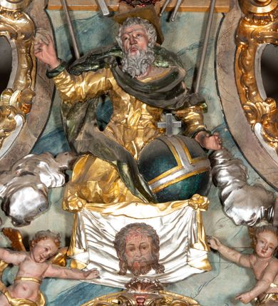 Zdjęcie nr 9: Ołtarz architektoniczny, trójosiowy, z wydzieloną częścią cokołową, jednokondygnacyjny, ze zwieńczeniem. Mensa drewniana tumbowa, ozdobiona nałożonymi płaskorzeźbionymi motywami rocaille’ów i roślinnymi. Po bokach mensy, w części cokołowej dwie bramki obejścia zamknięte półkoliście, w których osadzone na zawiasach drzwi jednoskrzydłowe z płycinami z malowanymi przedstawieniami świętych. W predelli oszklona trumienka z rzeźbą Chrystusa w grobie. Pole środkowe nastawy ujęte dwoma czworobocznymi filarami o kompozytowych kapitelach. Pola boczne wklęsłe i cofnięte od lica pola środkowego flankowane kolumnami o gładkich trzonach i kompozytowych kapitelach, umieszczonych na wysokich dwustopniowych postumentach ustawionych kątowo, zdobionych płycinami. Podpory dźwigają pełne belkowanie i gzyms, przerwane nad polem środkowym. W polu środkowym głęboka nisza w kształcie prostokąta stojącego zamkniętego łukiem wypukło-wklęsłym, w bogatym obramieniu. W niej rzeźba Pieta. Po bokach, na tle filarów, umieszczone dwa okazałe anioły w dynamicznych pozach, z rozłożonymi skrzydłami. Ponad niszą płaskorzeźbiona Chusta św. Weroniki rozpostarta przez dwa uskrzydlone putta ze stopami wspartymi na obłokach. W polach bocznych nastawy sferyczne płyciny w asymetrycznych złoconych obramieniach, na których tle umieszczone na konsolach rzeźby: Św. Jan Ewangelista (po lewej) i Św. Maria Magdalena (po prawej). Zwieńczenie w formie aedikuli ujętej wolutami i zwieńczonej półkoliście. Na tle aedikuli rzeźbione przedstawienie tronującego Boga Ojca, ponad głową którego Arma Christi; wokół putta i uskrzydlone główki aniołków. W osiach podpór rzeźby uskrzydlonych aniołów. Uszaki nastawy rzeźbione, ażurowe, złocone, z motywów rocaille’ów i kwiatów słonecznika. Struktura polichromowana na kolor szaro-niebieski, a trzony filarów i kolumn oraz tła płycin na czerwono, imitując marmur;  detale i ornamenty złocone; szaty rzeźb złocone i srebrzone; karnacje w kolorze naturalnym. 