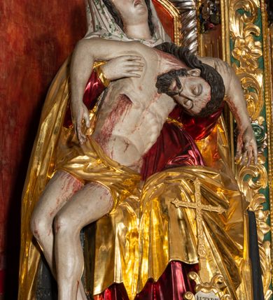 Zdjęcie nr 18: Ołtarz architektoniczny, trójosiowy, z wydzieloną częścią cokołową, jednokondygnacyjny, ze zwieńczeniem. Mensa drewniana tumbowa, ozdobiona nałożonymi płaskorzeźbionymi motywami rocaille’ów i roślinnymi. Po bokach mensy, w części cokołowej dwie bramki obejścia zamknięte półkoliście, w których osadzone na zawiasach drzwi jednoskrzydłowe z płycinami z malowanymi przedstawieniami świętych. W predelli oszklona trumienka z rzeźbą Chrystusa w grobie. Pole środkowe nastawy ujęte dwoma czworobocznymi filarami o kompozytowych kapitelach. Pola boczne wklęsłe i cofnięte od lica pola środkowego flankowane kolumnami o gładkich trzonach i kompozytowych kapitelach, umieszczonych na wysokich dwustopniowych postumentach ustawionych kątowo, zdobionych płycinami. Podpory dźwigają pełne belkowanie i gzyms, przerwane nad polem środkowym. W polu środkowym głęboka nisza w kształcie prostokąta stojącego zamkniętego łukiem wypukło-wklęsłym, w bogatym obramieniu. W niej rzeźba Pieta. Po bokach, na tle filarów, umieszczone dwa okazałe anioły w dynamicznych pozach, z rozłożonymi skrzydłami. Ponad niszą płaskorzeźbiona Chusta św. Weroniki rozpostarta przez dwa uskrzydlone putta ze stopami wspartymi na obłokach. W polach bocznych nastawy sferyczne płyciny w asymetrycznych złoconych obramieniach, na których tle umieszczone na konsolach rzeźby: Św. Jan Ewangelista (po lewej) i Św. Maria Magdalena (po prawej). Zwieńczenie w formie aedikuli ujętej wolutami i zwieńczonej półkoliście. Na tle aedikuli rzeźbione przedstawienie tronującego Boga Ojca, ponad głową którego Arma Christi; wokół putta i uskrzydlone główki aniołków. W osiach podpór rzeźby uskrzydlonych aniołów. Uszaki nastawy rzeźbione, ażurowe, złocone, z motywów rocaille’ów i kwiatów słonecznika. Struktura polichromowana na kolor szaro-niebieski, a trzony filarów i kolumn oraz tła płycin na czerwono, imitując marmur;  detale i ornamenty złocone; szaty rzeźb złocone i srebrzone; karnacje w kolorze naturalnym. 