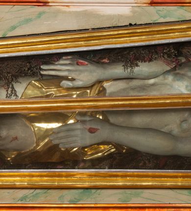 Zdjęcie nr 21: Ołtarz architektoniczny, trójosiowy, z wydzieloną częścią cokołową, jednokondygnacyjny, ze zwieńczeniem. Mensa drewniana tumbowa, ozdobiona nałożonymi płaskorzeźbionymi motywami rocaille’ów i roślinnymi. Po bokach mensy, w części cokołowej dwie bramki obejścia zamknięte półkoliście, w których osadzone na zawiasach drzwi jednoskrzydłowe z płycinami z malowanymi przedstawieniami świętych. W predelli oszklona trumienka z rzeźbą Chrystusa w grobie. Pole środkowe nastawy ujęte dwoma czworobocznymi filarami o kompozytowych kapitelach. Pola boczne wklęsłe i cofnięte od lica pola środkowego flankowane kolumnami o gładkich trzonach i kompozytowych kapitelach, umieszczonych na wysokich dwustopniowych postumentach ustawionych kątowo, zdobionych płycinami. Podpory dźwigają pełne belkowanie i gzyms, przerwane nad polem środkowym. W polu środkowym głęboka nisza w kształcie prostokąta stojącego zamkniętego łukiem wypukło-wklęsłym, w bogatym obramieniu. W niej rzeźba Pieta. Po bokach, na tle filarów, umieszczone dwa okazałe anioły w dynamicznych pozach, z rozłożonymi skrzydłami. Ponad niszą płaskorzeźbiona Chusta św. Weroniki rozpostarta przez dwa uskrzydlone putta ze stopami wspartymi na obłokach. W polach bocznych nastawy sferyczne płyciny w asymetrycznych złoconych obramieniach, na których tle umieszczone na konsolach rzeźby: Św. Jan Ewangelista (po lewej) i Św. Maria Magdalena (po prawej). Zwieńczenie w formie aedikuli ujętej wolutami i zwieńczonej półkoliście. Na tle aedikuli rzeźbione przedstawienie tronującego Boga Ojca, ponad głową którego Arma Christi; wokół putta i uskrzydlone główki aniołków. W osiach podpór rzeźby uskrzydlonych aniołów. Uszaki nastawy rzeźbione, ażurowe, złocone, z motywów rocaille’ów i kwiatów słonecznika. Struktura polichromowana na kolor szaro-niebieski, a trzony filarów i kolumn oraz tła płycin na czerwono, imitując marmur;  detale i ornamenty złocone; szaty rzeźb złocone i srebrzone; karnacje w kolorze naturalnym. 