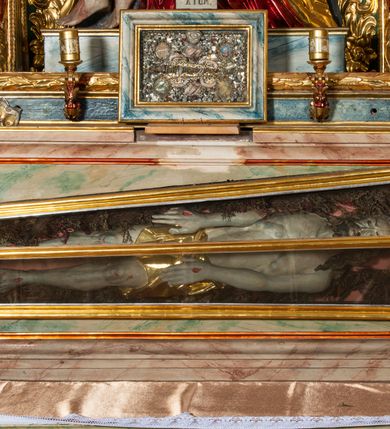 Zdjęcie nr 20: Ołtarz architektoniczny, trójosiowy, z wydzieloną częścią cokołową, jednokondygnacyjny, ze zwieńczeniem. Mensa drewniana tumbowa, ozdobiona nałożonymi płaskorzeźbionymi motywami rocaille’ów i roślinnymi. Po bokach mensy, w części cokołowej dwie bramki obejścia zamknięte półkoliście, w których osadzone na zawiasach drzwi jednoskrzydłowe z płycinami z malowanymi przedstawieniami świętych. W predelli oszklona trumienka z rzeźbą Chrystusa w grobie. Pole środkowe nastawy ujęte dwoma czworobocznymi filarami o kompozytowych kapitelach. Pola boczne wklęsłe i cofnięte od lica pola środkowego flankowane kolumnami o gładkich trzonach i kompozytowych kapitelach, umieszczonych na wysokich dwustopniowych postumentach ustawionych kątowo, zdobionych płycinami. Podpory dźwigają pełne belkowanie i gzyms, przerwane nad polem środkowym. W polu środkowym głęboka nisza w kształcie prostokąta stojącego zamkniętego łukiem wypukło-wklęsłym, w bogatym obramieniu. W niej rzeźba Pieta. Po bokach, na tle filarów, umieszczone dwa okazałe anioły w dynamicznych pozach, z rozłożonymi skrzydłami. Ponad niszą płaskorzeźbiona Chusta św. Weroniki rozpostarta przez dwa uskrzydlone putta ze stopami wspartymi na obłokach. W polach bocznych nastawy sferyczne płyciny w asymetrycznych złoconych obramieniach, na których tle umieszczone na konsolach rzeźby: Św. Jan Ewangelista (po lewej) i Św. Maria Magdalena (po prawej). Zwieńczenie w formie aedikuli ujętej wolutami i zwieńczonej półkoliście. Na tle aedikuli rzeźbione przedstawienie tronującego Boga Ojca, ponad głową którego Arma Christi; wokół putta i uskrzydlone główki aniołków. W osiach podpór rzeźby uskrzydlonych aniołów. Uszaki nastawy rzeźbione, ażurowe, złocone, z motywów rocaille’ów i kwiatów słonecznika. Struktura polichromowana na kolor szaro-niebieski, a trzony filarów i kolumn oraz tła płycin na czerwono, imitując marmur;  detale i ornamenty złocone; szaty rzeźb złocone i srebrzone; karnacje w kolorze naturalnym. 