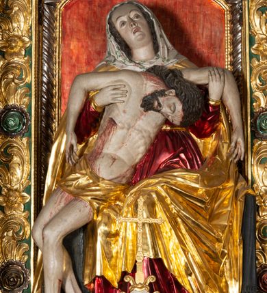 Zdjęcie nr 13: Ołtarz architektoniczny, trójosiowy, z wydzieloną częścią cokołową, jednokondygnacyjny, ze zwieńczeniem. Mensa drewniana tumbowa, ozdobiona nałożonymi płaskorzeźbionymi motywami rocaille’ów i roślinnymi. Po bokach mensy, w części cokołowej dwie bramki obejścia zamknięte półkoliście, w których osadzone na zawiasach drzwi jednoskrzydłowe z płycinami z malowanymi przedstawieniami świętych. W predelli oszklona trumienka z rzeźbą Chrystusa w grobie. Pole środkowe nastawy ujęte dwoma czworobocznymi filarami o kompozytowych kapitelach. Pola boczne wklęsłe i cofnięte od lica pola środkowego flankowane kolumnami o gładkich trzonach i kompozytowych kapitelach, umieszczonych na wysokich dwustopniowych postumentach ustawionych kątowo, zdobionych płycinami. Podpory dźwigają pełne belkowanie i gzyms, przerwane nad polem środkowym. W polu środkowym głęboka nisza w kształcie prostokąta stojącego zamkniętego łukiem wypukło-wklęsłym, w bogatym obramieniu. W niej rzeźba Pieta. Po bokach, na tle filarów, umieszczone dwa okazałe anioły w dynamicznych pozach, z rozłożonymi skrzydłami. Ponad niszą płaskorzeźbiona Chusta św. Weroniki rozpostarta przez dwa uskrzydlone putta ze stopami wspartymi na obłokach. W polach bocznych nastawy sferyczne płyciny w asymetrycznych złoconych obramieniach, na których tle umieszczone na konsolach rzeźby: Św. Jan Ewangelista (po lewej) i Św. Maria Magdalena (po prawej). Zwieńczenie w formie aedikuli ujętej wolutami i zwieńczonej półkoliście. Na tle aedikuli rzeźbione przedstawienie tronującego Boga Ojca, ponad głową którego Arma Christi; wokół putta i uskrzydlone główki aniołków. W osiach podpór rzeźby uskrzydlonych aniołów. Uszaki nastawy rzeźbione, ażurowe, złocone, z motywów rocaille’ów i kwiatów słonecznika. Struktura polichromowana na kolor szaro-niebieski, a trzony filarów i kolumn oraz tła płycin na czerwono, imitując marmur;  detale i ornamenty złocone; szaty rzeźb złocone i srebrzone; karnacje w kolorze naturalnym. 