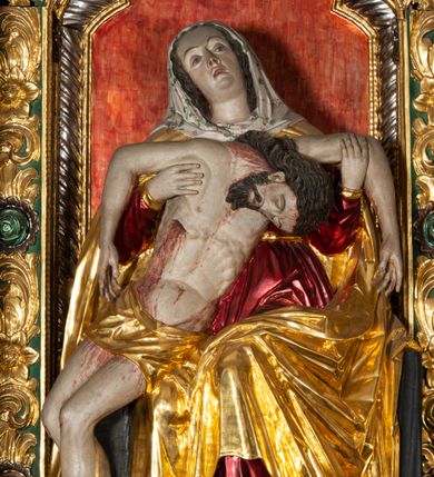 Zdjęcie nr 14: Ołtarz architektoniczny, trójosiowy, z wydzieloną częścią cokołową, jednokondygnacyjny, ze zwieńczeniem. Mensa drewniana tumbowa, ozdobiona nałożonymi płaskorzeźbionymi motywami rocaille’ów i roślinnymi. Po bokach mensy, w części cokołowej dwie bramki obejścia zamknięte półkoliście, w których osadzone na zawiasach drzwi jednoskrzydłowe z płycinami z malowanymi przedstawieniami świętych. W predelli oszklona trumienka z rzeźbą Chrystusa w grobie. Pole środkowe nastawy ujęte dwoma czworobocznymi filarami o kompozytowych kapitelach. Pola boczne wklęsłe i cofnięte od lica pola środkowego flankowane kolumnami o gładkich trzonach i kompozytowych kapitelach, umieszczonych na wysokich dwustopniowych postumentach ustawionych kątowo, zdobionych płycinami. Podpory dźwigają pełne belkowanie i gzyms, przerwane nad polem środkowym. W polu środkowym głęboka nisza w kształcie prostokąta stojącego zamkniętego łukiem wypukło-wklęsłym, w bogatym obramieniu. W niej rzeźba Pieta. Po bokach, na tle filarów, umieszczone dwa okazałe anioły w dynamicznych pozach, z rozłożonymi skrzydłami. Ponad niszą płaskorzeźbiona Chusta św. Weroniki rozpostarta przez dwa uskrzydlone putta ze stopami wspartymi na obłokach. W polach bocznych nastawy sferyczne płyciny w asymetrycznych złoconych obramieniach, na których tle umieszczone na konsolach rzeźby: Św. Jan Ewangelista (po lewej) i Św. Maria Magdalena (po prawej). Zwieńczenie w formie aedikuli ujętej wolutami i zwieńczonej półkoliście. Na tle aedikuli rzeźbione przedstawienie tronującego Boga Ojca, ponad głową którego Arma Christi; wokół putta i uskrzydlone główki aniołków. W osiach podpór rzeźby uskrzydlonych aniołów. Uszaki nastawy rzeźbione, ażurowe, złocone, z motywów rocaille’ów i kwiatów słonecznika. Struktura polichromowana na kolor szaro-niebieski, a trzony filarów i kolumn oraz tła płycin na czerwono, imitując marmur;  detale i ornamenty złocone; szaty rzeźb złocone i srebrzone; karnacje w kolorze naturalnym. 