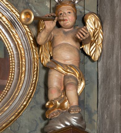 Zdjęcie nr 12: Prospekt organowy jednokondygnacyjny, trójosiowy, złożony z trzech prostopadłościennych segmentów z ryzalitami; środkowy najwyższy, na rzucie półkolisty, skrajne niższe, dwuboczne, dźwigające odcinki belkowania i profilowanego gzymsu; w zwieńczeniu owalne medaliony ujęte liśćmi akantu. Ryzality wypełnione piszczałkami, częściowo przesłoniętymi ażurową dekoracją. Prospekt ujęty ażurowymi uszakami z motywów roślinnych. Struktura polichromowana w kolorze drewna, ornamenty złocone.
