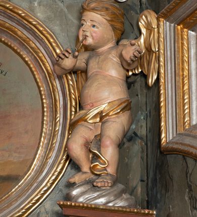 Zdjęcie nr 10: Prospekt organowy jednokondygnacyjny, trójosiowy, złożony z trzech prostopadłościennych segmentów z ryzalitami; środkowy najwyższy, na rzucie półkolisty, skrajne niższe, dwuboczne, dźwigające odcinki belkowania i profilowanego gzymsu; w zwieńczeniu owalne medaliony ujęte liśćmi akantu. Ryzality wypełnione piszczałkami, częściowo przesłoniętymi ażurową dekoracją. Prospekt ujęty ażurowymi uszakami z motywów roślinnych. Struktura polichromowana w kolorze drewna, ornamenty złocone.
