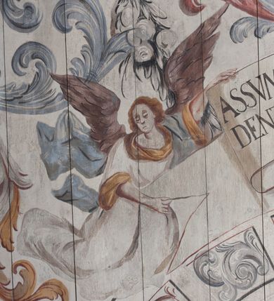 Zdjęcie nr 18: Polichromia umieszczona na stropie nawy głównej. W polu środkowym scena Wniebowzięcia Najświętszej Marii Panny umieszczona w kwadratowej ramie o bokach zamkniętych łukami nadwieszonymi. Rama profilowana, zdobiona rzędem pojedynczych liści. Matka Boska unosząca się na obłokach z szeroko rozłożonymi na boki rękami, prawą wzniesioną do góry. Twarz owalna z długim nosem, silnie zaciśniętymi ustami i dużymi oczami, skierowanymi ku górze. Włosy jasne, kręcone, schowane pod żółtym welonem, którego jeden koniec rozwiany jest wzdłuż prawej ręki. Matka Boska ubrana jest w szeroką, różową suknię, przewiązaną w talii pomarańczową tasiemką oraz błękitny płaszcz, założony za lewe ramię i rozwiany z tyłu. Nad głową Matki Boskiej aniołki unoszą insygnia królewskie: koronę, berło, a także gałązkę białej lilii. Poniżej grupy aniołów podtrzymujące obłoki. Dokoła ramy bujne sploty różnokolorowego akantu przeplecionego karbowaną wstęgą, owijające również ramę ze sceną Wniebowzięcia. W dolnej części ukazane są ponadto dwa anioły podtrzymujące białą wstęgę z napisem: „ASSVMPTA EST MARIA IN COELVM, GAV, / DENT ANGELI, LAVDANTES BENEDICVNT / DOMINVM.” Z kolei z drugiej strony stropu umieszczony jest owalny medalion, obwiedziony liśćmi wawrzynu, w polu którego umieszczone jest czerwone godło zakonu Bożogrobowców oraz małe uskrzydlone główki aniołków. Powyżej na białej wstędze umieszczony jest napis: „SVB HOC SIGNO.”, a poniżej: „RESTAVRATVM A(NN)O (DOMINI) 1714 / Die 14 Aug(st)”. Całość stropu obwiedziona jest dookoła pasem przeważnie prostokątnych kasetonów, wypełnionych różnokolorowymi liśćmi akantu, a także od zewnątrz szerokim pasem dekoracyjnym z brązowych liści wawrzynu. Pasy na bokach wyłamane półkolistymi wypustkami, w których umieszczone są duże muszle palmetowe. Kolorystyka stonowana, jasna z przewagą błękitu i czerwieni.