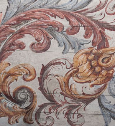 Zdjęcie nr 6: Polichromia umieszczona na stropie nawy głównej. W polu środkowym scena Wniebowzięcia Najświętszej Marii Panny umieszczona w kwadratowej ramie o bokach zamkniętych łukami nadwieszonymi. Rama profilowana, zdobiona rzędem pojedynczych liści. Matka Boska unosząca się na obłokach z szeroko rozłożonymi na boki rękami, prawą wzniesioną do góry. Twarz owalna z długim nosem, silnie zaciśniętymi ustami i dużymi oczami, skierowanymi ku górze. Włosy jasne, kręcone, schowane pod żółtym welonem, którego jeden koniec rozwiany jest wzdłuż prawej ręki. Matka Boska ubrana jest w szeroką, różową suknię, przewiązaną w talii pomarańczową tasiemką oraz błękitny płaszcz, założony za lewe ramię i rozwiany z tyłu. Nad głową Matki Boskiej aniołki unoszą insygnia królewskie: koronę, berło, a także gałązkę białej lilii. Poniżej grupy aniołów podtrzymujące obłoki. Dokoła ramy bujne sploty różnokolorowego akantu przeplecionego karbowaną wstęgą, owijające również ramę ze sceną Wniebowzięcia. W dolnej części ukazane są ponadto dwa anioły podtrzymujące białą wstęgę z napisem: „ASSVMPTA EST MARIA IN COELVM, GAV, / DENT ANGELI, LAVDANTES BENEDICVNT / DOMINVM.” Z kolei z drugiej strony stropu umieszczony jest owalny medalion, obwiedziony liśćmi wawrzynu, w polu którego umieszczone jest czerwone godło zakonu Bożogrobowców oraz małe uskrzydlone główki aniołków. Powyżej na białej wstędze umieszczony jest napis: „SVB HOC SIGNO.”, a poniżej: „RESTAVRATVM A(NN)O (DOMINI) 1714 / Die 14 Aug(st)”. Całość stropu obwiedziona jest dookoła pasem przeważnie prostokątnych kasetonów, wypełnionych różnokolorowymi liśćmi akantu, a także od zewnątrz szerokim pasem dekoracyjnym z brązowych liści wawrzynu. Pasy na bokach wyłamane półkolistymi wypustkami, w których umieszczone są duże muszle palmetowe. Kolorystyka stonowana, jasna z przewagą błękitu i czerwieni.