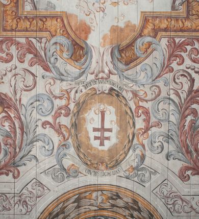 Zdjęcie nr 16: Polichromia umieszczona na stropie nawy głównej. W polu środkowym scena Wniebowzięcia Najświętszej Marii Panny umieszczona w kwadratowej ramie o bokach zamkniętych łukami nadwieszonymi. Rama profilowana, zdobiona rzędem pojedynczych liści. Matka Boska unosząca się na obłokach z szeroko rozłożonymi na boki rękami, prawą wzniesioną do góry. Twarz owalna z długim nosem, silnie zaciśniętymi ustami i dużymi oczami, skierowanymi ku górze. Włosy jasne, kręcone, schowane pod żółtym welonem, którego jeden koniec rozwiany jest wzdłuż prawej ręki. Matka Boska ubrana jest w szeroką, różową suknię, przewiązaną w talii pomarańczową tasiemką oraz błękitny płaszcz, założony za lewe ramię i rozwiany z tyłu. Nad głową Matki Boskiej aniołki unoszą insygnia królewskie: koronę, berło, a także gałązkę białej lilii. Poniżej grupy aniołów podtrzymujące obłoki. Dokoła ramy bujne sploty różnokolorowego akantu przeplecionego karbowaną wstęgą, owijające również ramę ze sceną Wniebowzięcia. W dolnej części ukazane są ponadto dwa anioły podtrzymujące białą wstęgę z napisem: „ASSVMPTA EST MARIA IN COELVM, GAV, / DENT ANGELI, LAVDANTES BENEDICVNT / DOMINVM.” Z kolei z drugiej strony stropu umieszczony jest owalny medalion, obwiedziony liśćmi wawrzynu, w polu którego umieszczone jest czerwone godło zakonu Bożogrobowców oraz małe uskrzydlone główki aniołków. Powyżej na białej wstędze umieszczony jest napis: „SVB HOC SIGNO.”, a poniżej: „RESTAVRATVM A(NN)O (DOMINI) 1714 / Die 14 Aug(st)”. Całość stropu obwiedziona jest dookoła pasem przeważnie prostokątnych kasetonów, wypełnionych różnokolorowymi liśćmi akantu, a także od zewnątrz szerokim pasem dekoracyjnym z brązowych liści wawrzynu. Pasy na bokach wyłamane półkolistymi wypustkami, w których umieszczone są duże muszle palmetowe. Kolorystyka stonowana, jasna z przewagą błękitu i czerwieni.