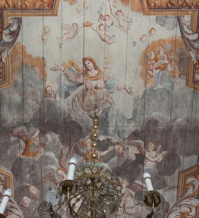 Zdjęcie nr 2: Polichromia umieszczona na stropie nawy głównej. W polu środkowym scena Wniebowzięcia Najświętszej Marii Panny umieszczona w kwadratowej ramie o bokach zamkniętych łukami nadwieszonymi. Rama profilowana, zdobiona rzędem pojedynczych liści. Matka Boska unosząca się na obłokach z szeroko rozłożonymi na boki rękami, prawą wzniesioną do góry. Twarz owalna z długim nosem, silnie zaciśniętymi ustami i dużymi oczami, skierowanymi ku górze. Włosy jasne, kręcone, schowane pod żółtym welonem, którego jeden koniec rozwiany jest wzdłuż prawej ręki. Matka Boska ubrana jest w szeroką, różową suknię, przewiązaną w talii pomarańczową tasiemką oraz błękitny płaszcz, założony za lewe ramię i rozwiany z tyłu. Nad głową Matki Boskiej aniołki unoszą insygnia królewskie: koronę, berło, a także gałązkę białej lilii. Poniżej grupy aniołów podtrzymujące obłoki. Dokoła ramy bujne sploty różnokolorowego akantu przeplecionego karbowaną wstęgą, owijające również ramę ze sceną Wniebowzięcia. W dolnej części ukazane są ponadto dwa anioły podtrzymujące białą wstęgę z napisem: „ASSVMPTA EST MARIA IN COELVM, GAV, / DENT ANGELI, LAVDANTES BENEDICVNT / DOMINVM.” Z kolei z drugiej strony stropu umieszczony jest owalny medalion, obwiedziony liśćmi wawrzynu, w polu którego umieszczone jest czerwone godło zakonu Bożogrobowców oraz małe uskrzydlone główki aniołków. Powyżej na białej wstędze umieszczony jest napis: „SVB HOC SIGNO.”, a poniżej: „RESTAVRATVM A(NN)O (DOMINI) 1714 / Die 14 Aug(st)”. Całość stropu obwiedziona jest dookoła pasem przeważnie prostokątnych kasetonów, wypełnionych różnokolorowymi liśćmi akantu, a także od zewnątrz szerokim pasem dekoracyjnym z brązowych liści wawrzynu. Pasy na bokach wyłamane półkolistymi wypustkami, w których umieszczone są duże muszle palmetowe. Kolorystyka stonowana, jasna z przewagą błękitu i czerwieni.