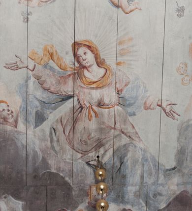 Zdjęcie nr 5: Polichromia umieszczona na stropie nawy głównej. W polu środkowym scena Wniebowzięcia Najświętszej Marii Panny umieszczona w kwadratowej ramie o bokach zamkniętych łukami nadwieszonymi. Rama profilowana, zdobiona rzędem pojedynczych liści. Matka Boska unosząca się na obłokach z szeroko rozłożonymi na boki rękami, prawą wzniesioną do góry. Twarz owalna z długim nosem, silnie zaciśniętymi ustami i dużymi oczami, skierowanymi ku górze. Włosy jasne, kręcone, schowane pod żółtym welonem, którego jeden koniec rozwiany jest wzdłuż prawej ręki. Matka Boska ubrana jest w szeroką, różową suknię, przewiązaną w talii pomarańczową tasiemką oraz błękitny płaszcz, założony za lewe ramię i rozwiany z tyłu. Nad głową Matki Boskiej aniołki unoszą insygnia królewskie: koronę, berło, a także gałązkę białej lilii. Poniżej grupy aniołów podtrzymujące obłoki. Dokoła ramy bujne sploty różnokolorowego akantu przeplecionego karbowaną wstęgą, owijające również ramę ze sceną Wniebowzięcia. W dolnej części ukazane są ponadto dwa anioły podtrzymujące białą wstęgę z napisem: „ASSVMPTA EST MARIA IN COELVM, GAV, / DENT ANGELI, LAVDANTES BENEDICVNT / DOMINVM.” Z kolei z drugiej strony stropu umieszczony jest owalny medalion, obwiedziony liśćmi wawrzynu, w polu którego umieszczone jest czerwone godło zakonu Bożogrobowców oraz małe uskrzydlone główki aniołków. Powyżej na białej wstędze umieszczony jest napis: „SVB HOC SIGNO.”, a poniżej: „RESTAVRATVM A(NN)O (DOMINI) 1714 / Die 14 Aug(st)”. Całość stropu obwiedziona jest dookoła pasem przeważnie prostokątnych kasetonów, wypełnionych różnokolorowymi liśćmi akantu, a także od zewnątrz szerokim pasem dekoracyjnym z brązowych liści wawrzynu. Pasy na bokach wyłamane półkolistymi wypustkami, w których umieszczone są duże muszle palmetowe. Kolorystyka stonowana, jasna z przewagą błękitu i czerwieni.